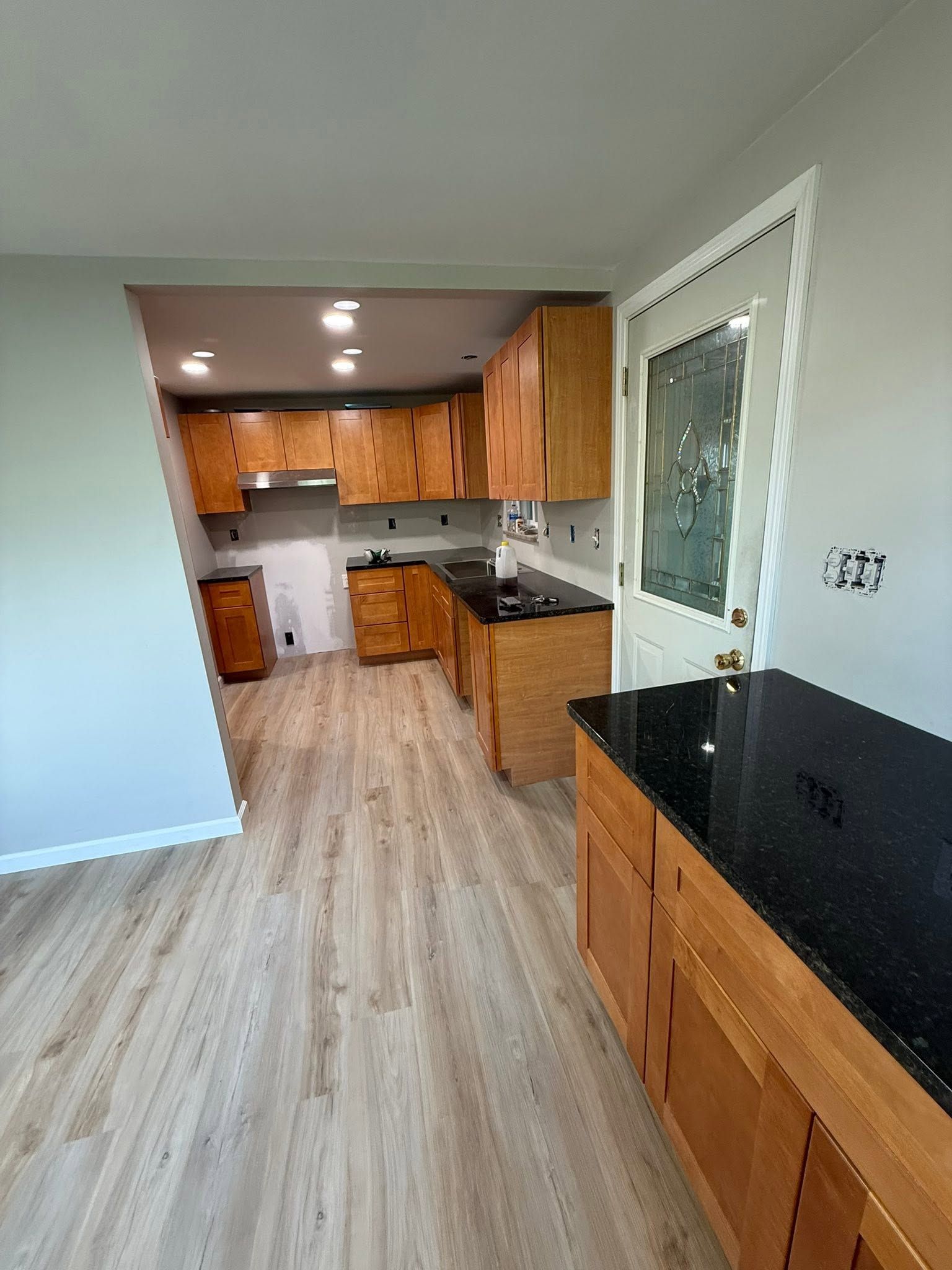 Empty kitchen and dining area with wood cabinets, black countertops, and light wood flooring