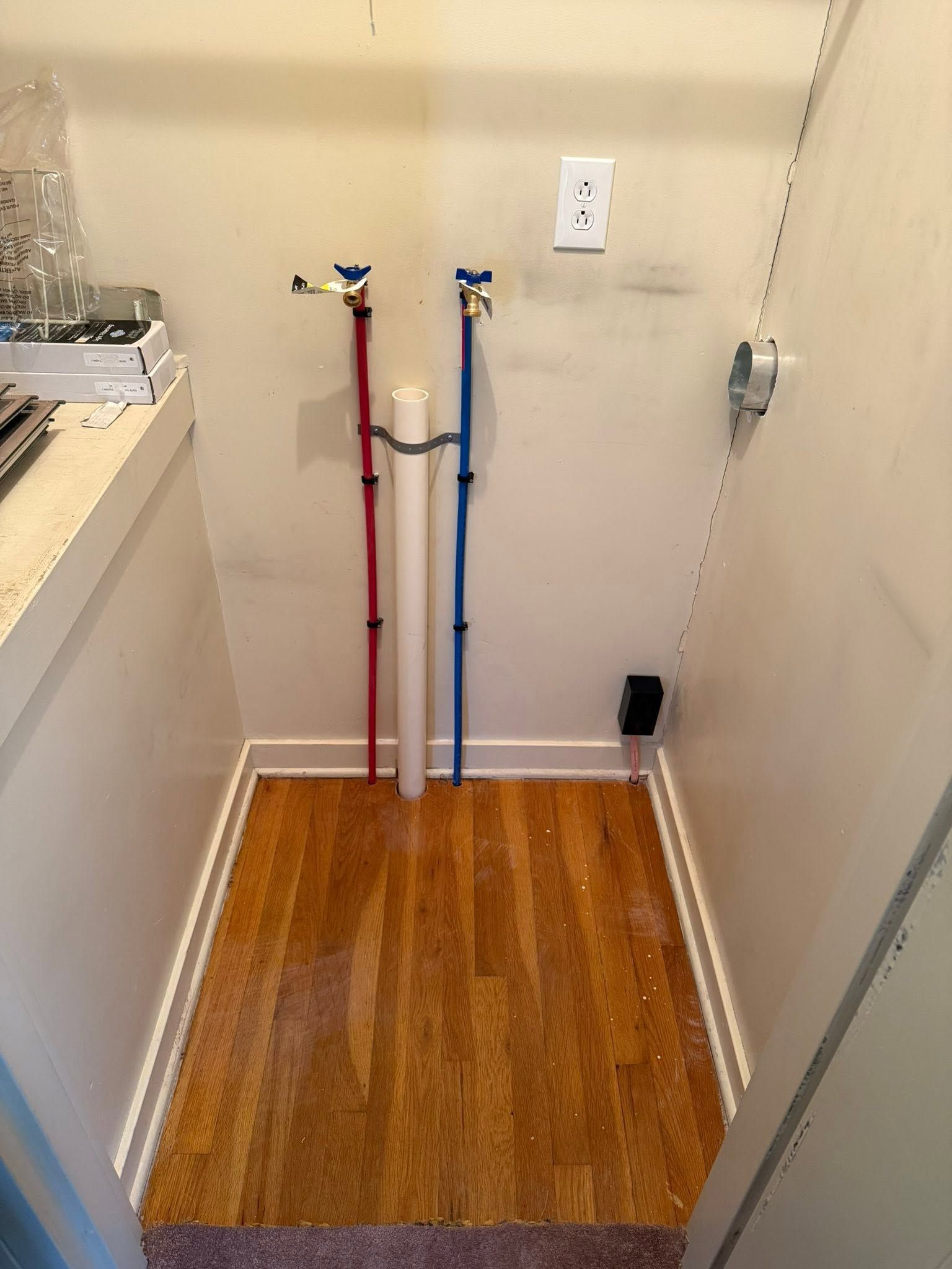 Laundry room with red and blue water supply lines and hookups above a wood floor.