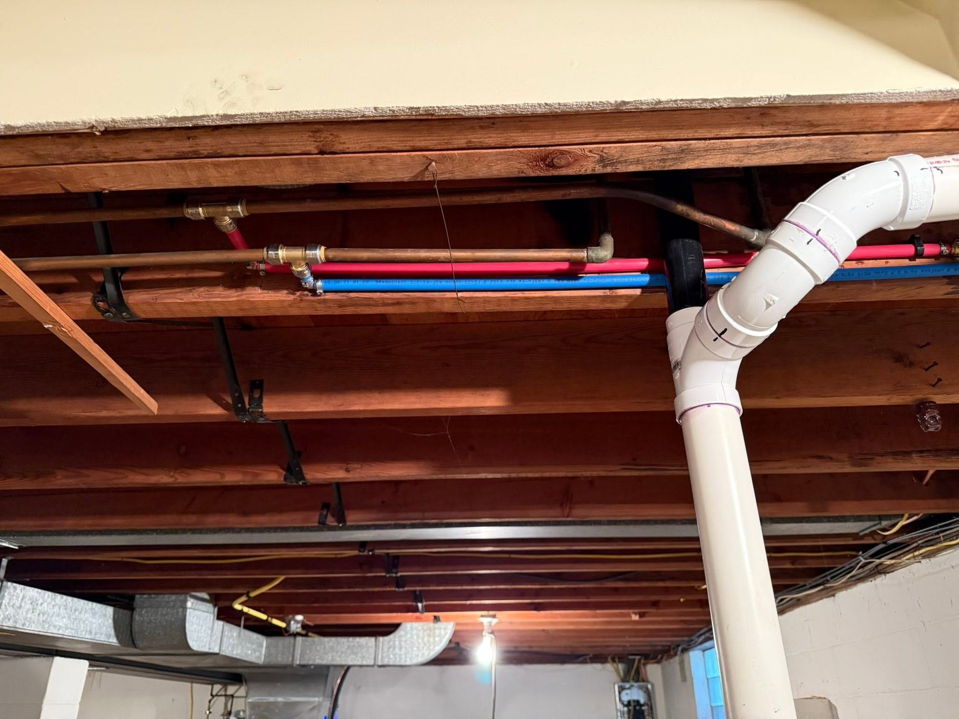 Exposed basement ceiling with copper pipes and a white PVC drainpipe
