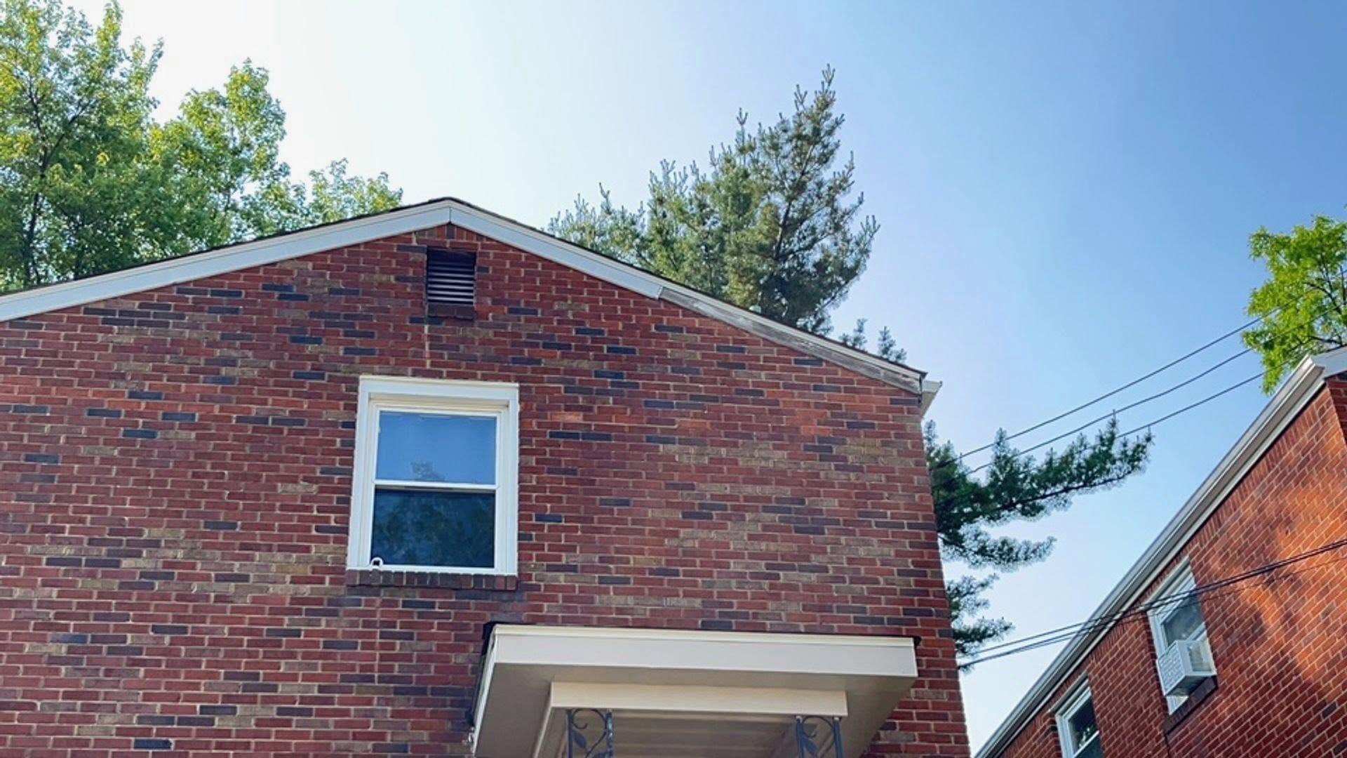 Red brick house exterior with a white-trimmed window and blue sky above