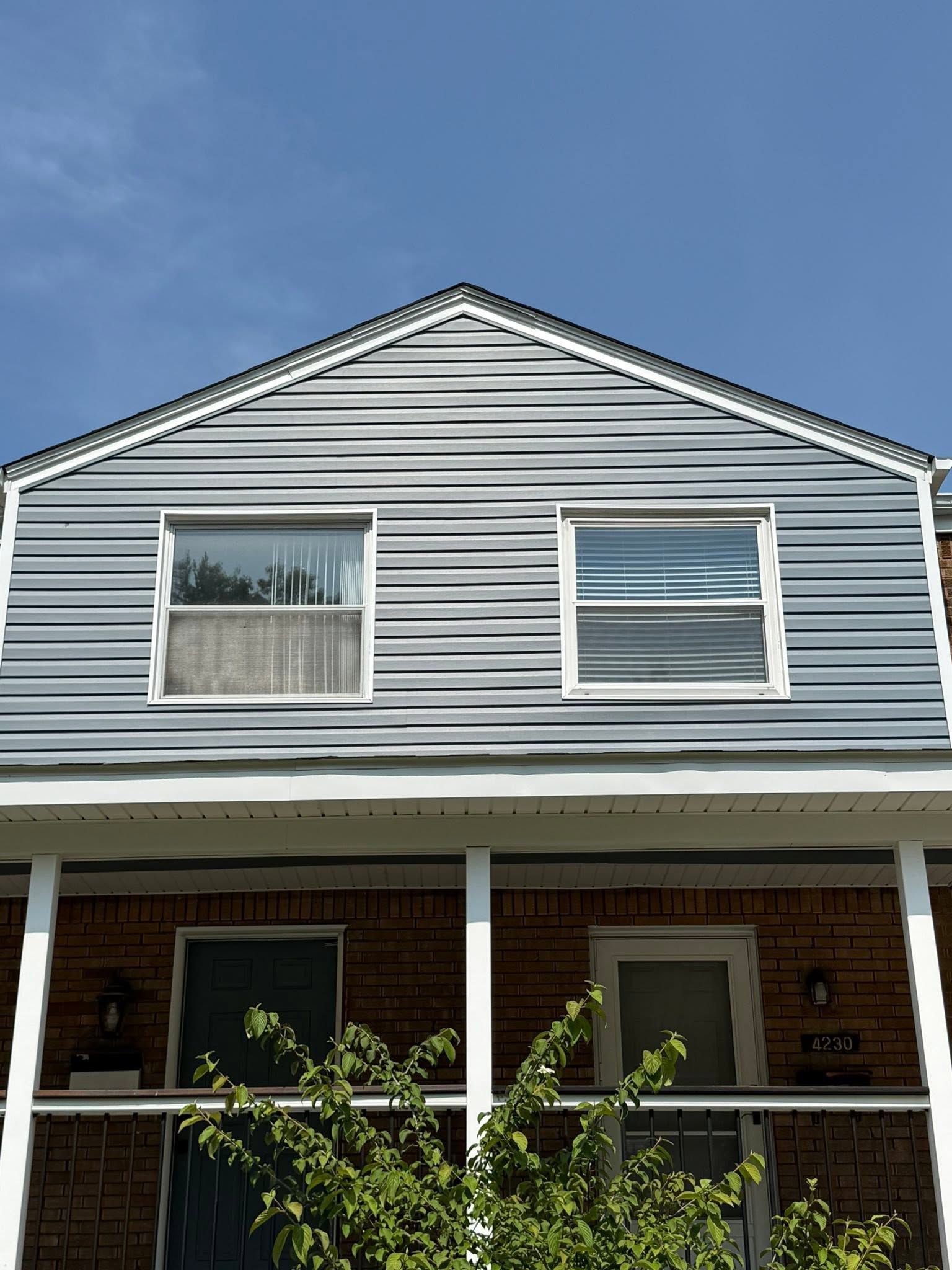 Two-story house with gray siding, white trim, and a front porch under a blue sky.