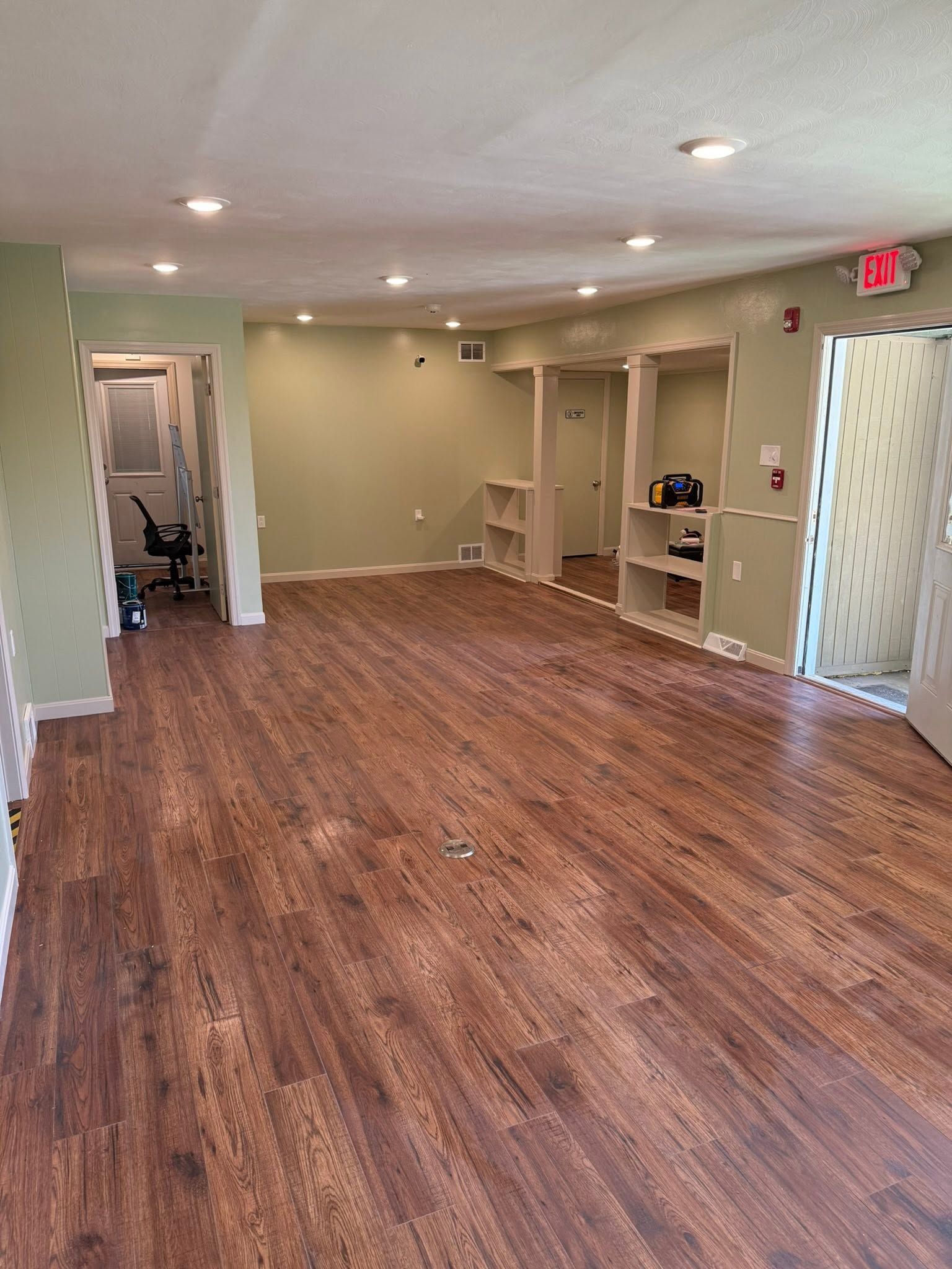 Empty office space with wood flooring, recessed lights, and built-in shelving near a doorway.