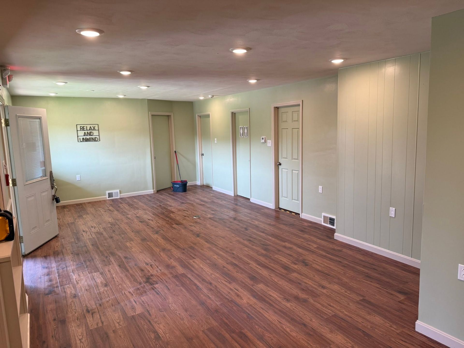 Empty living room with wood flooring, beige walls, recessed lights, and multiple white doors.
