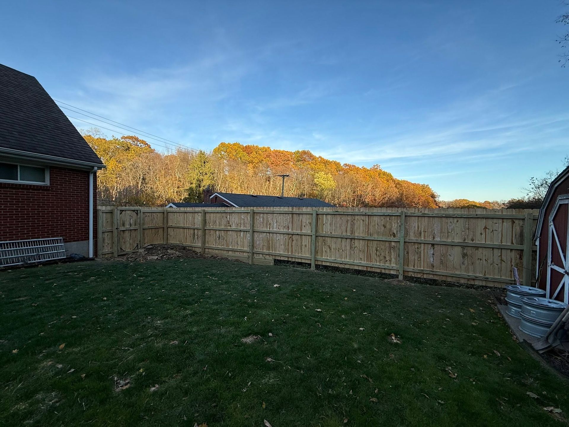 Backyard with wooden fence, green lawn, and autumn trees under a clear blue sky