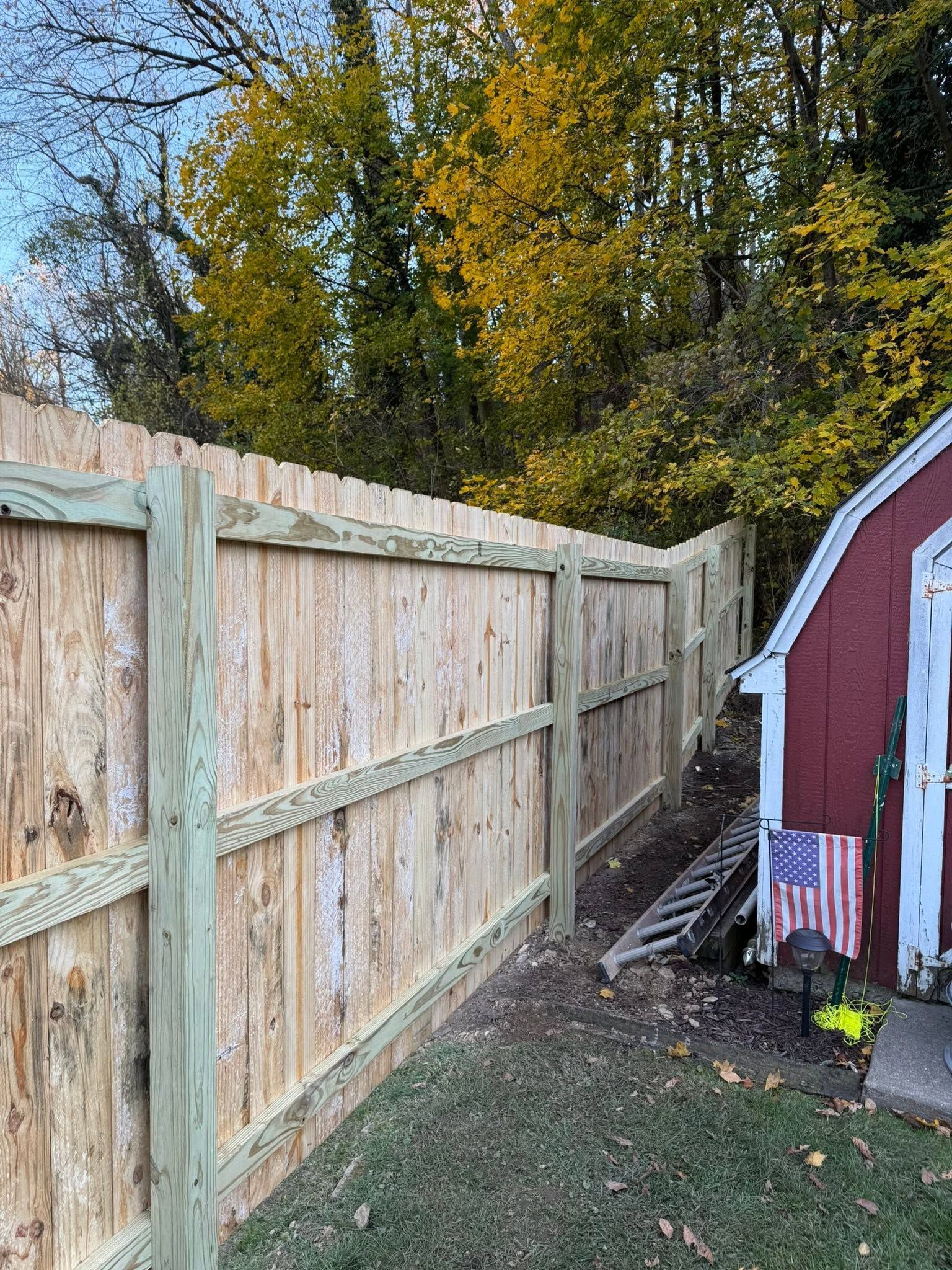 Wooden fence beside a red shed, with autumn trees and leaves in the background