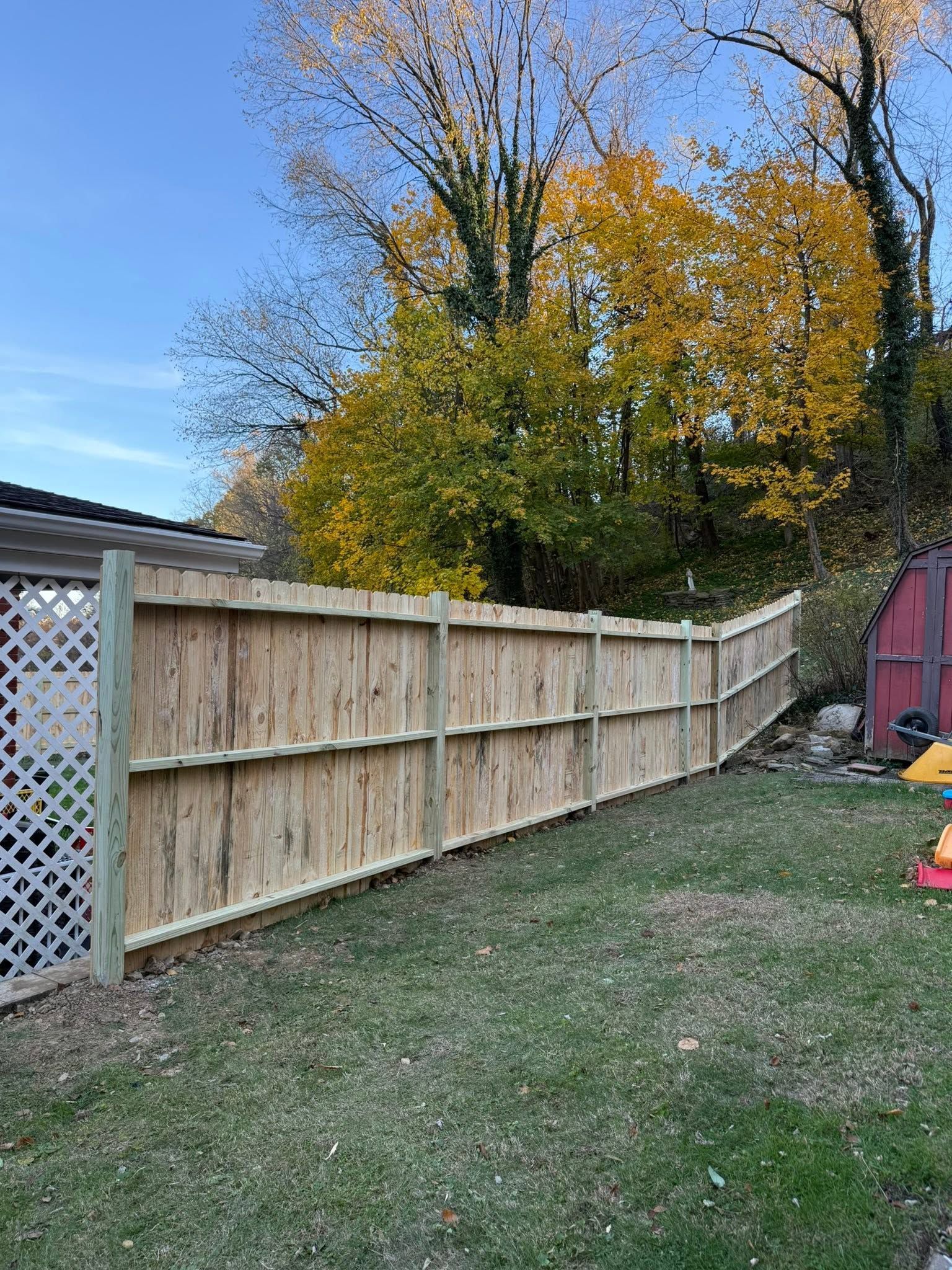 Curved wooden backyard fence with lattice gate, grass lawn, and autumn trees under a blue sky