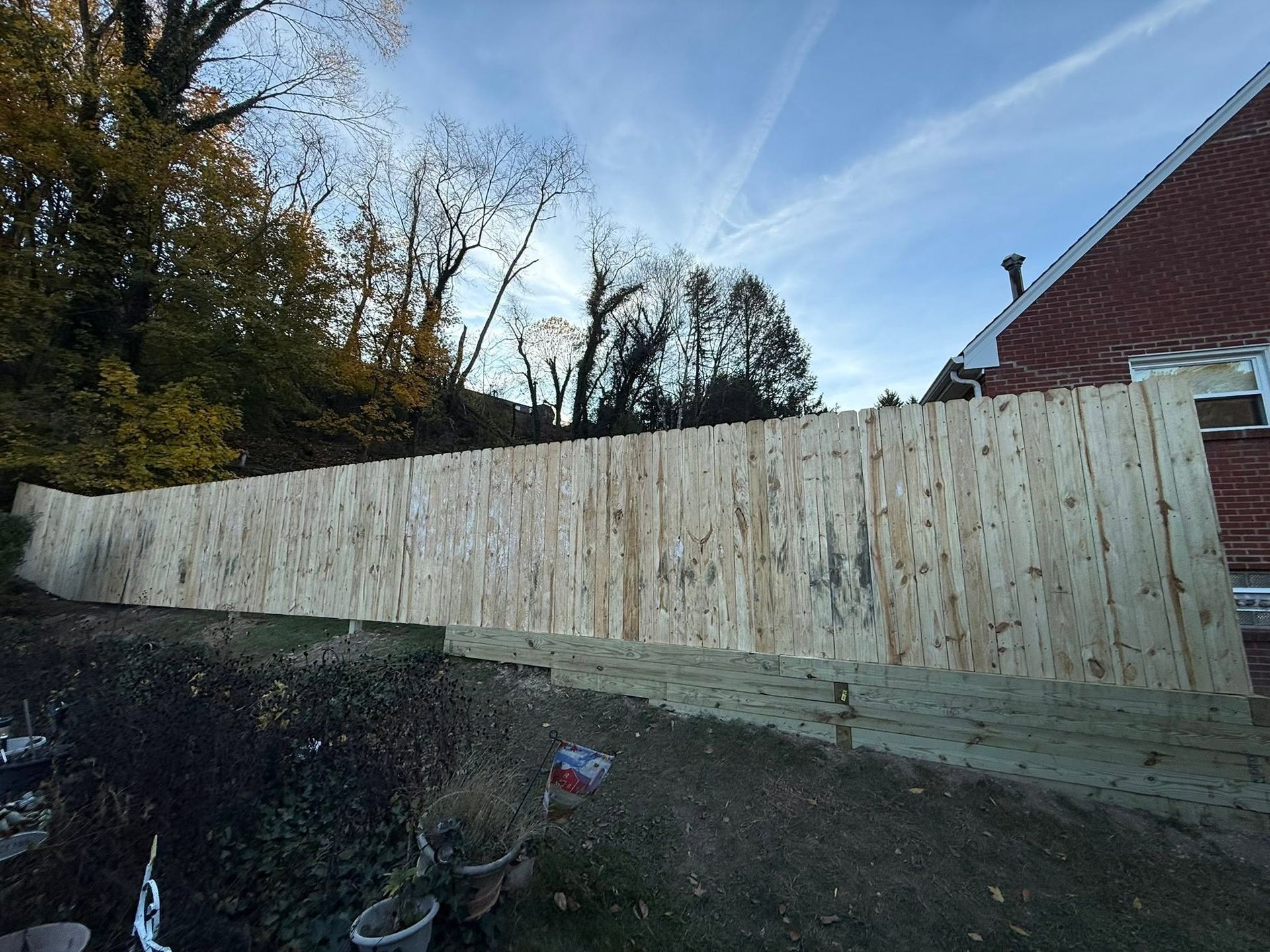 Long wooden fence beside a driveway and brick house under a blue sky