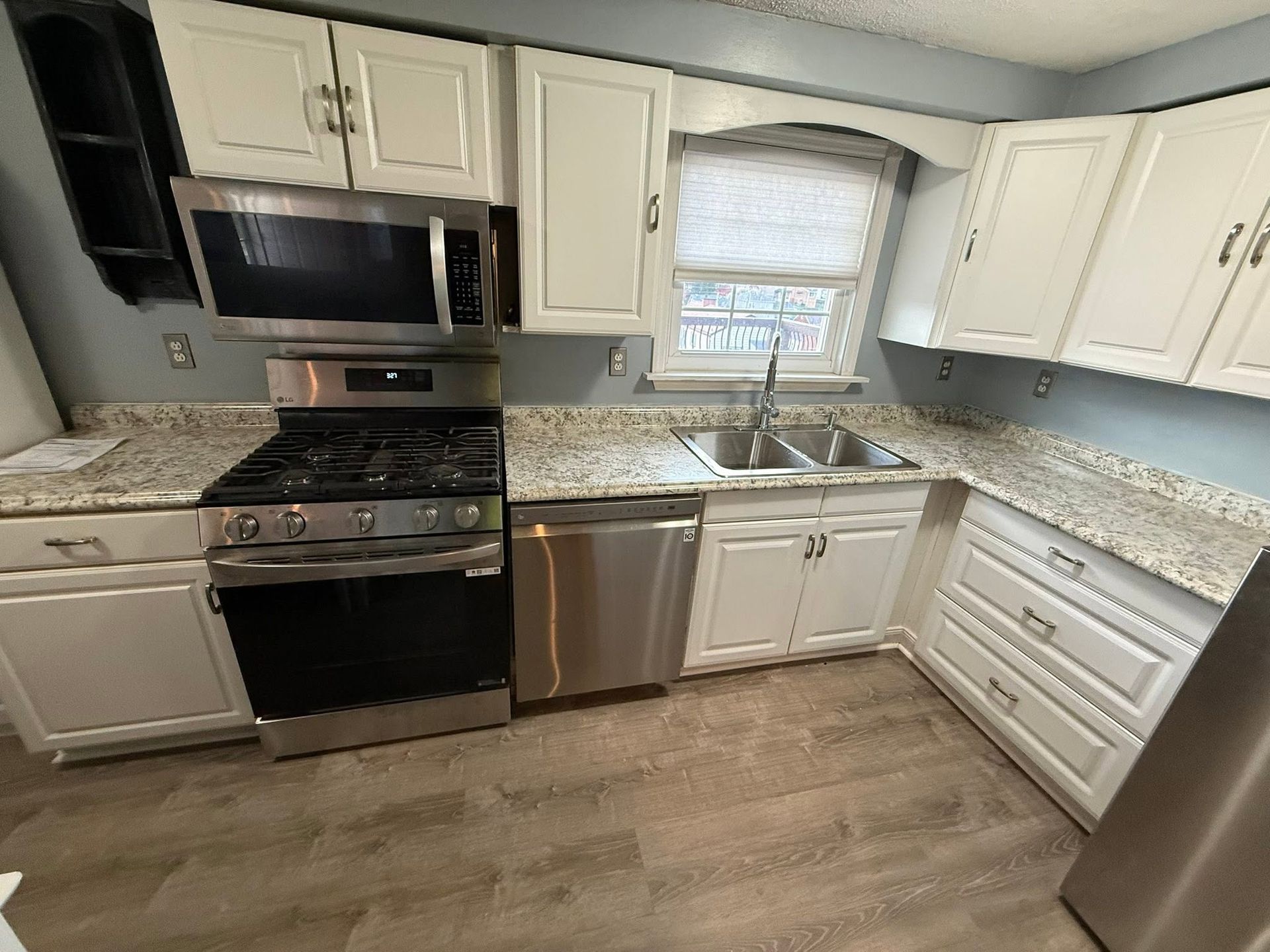 Modern kitchen with white cabinets, stainless appliances, granite counters, and wood-look flooring.