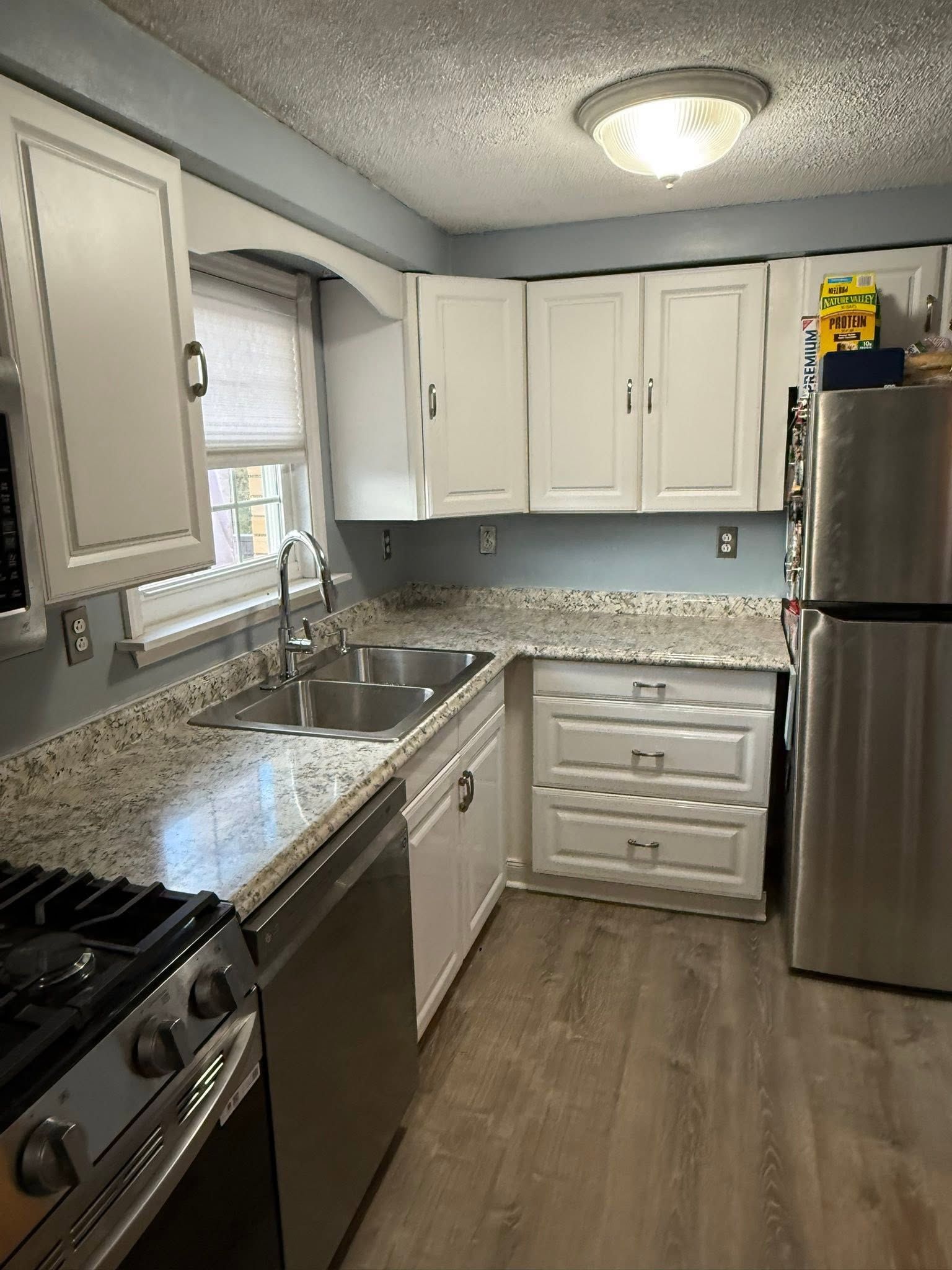 Bright kitchen with white cabinets, granite counters, stainless appliances, and a window over the sink.