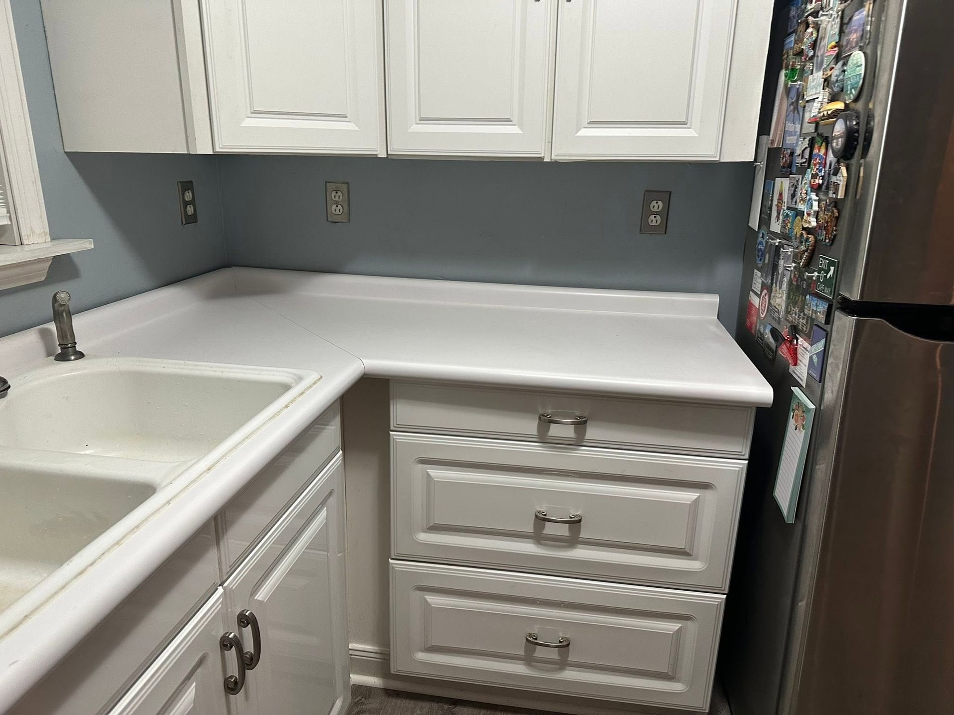 White kitchen with sink, cabinets, and drawers beside a countertop and refrigerator.