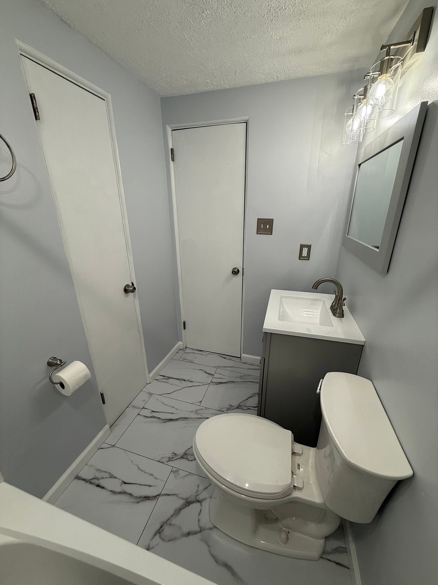 Small bathroom with toilet, sink, mirror, and marble-pattern floor in gray tones