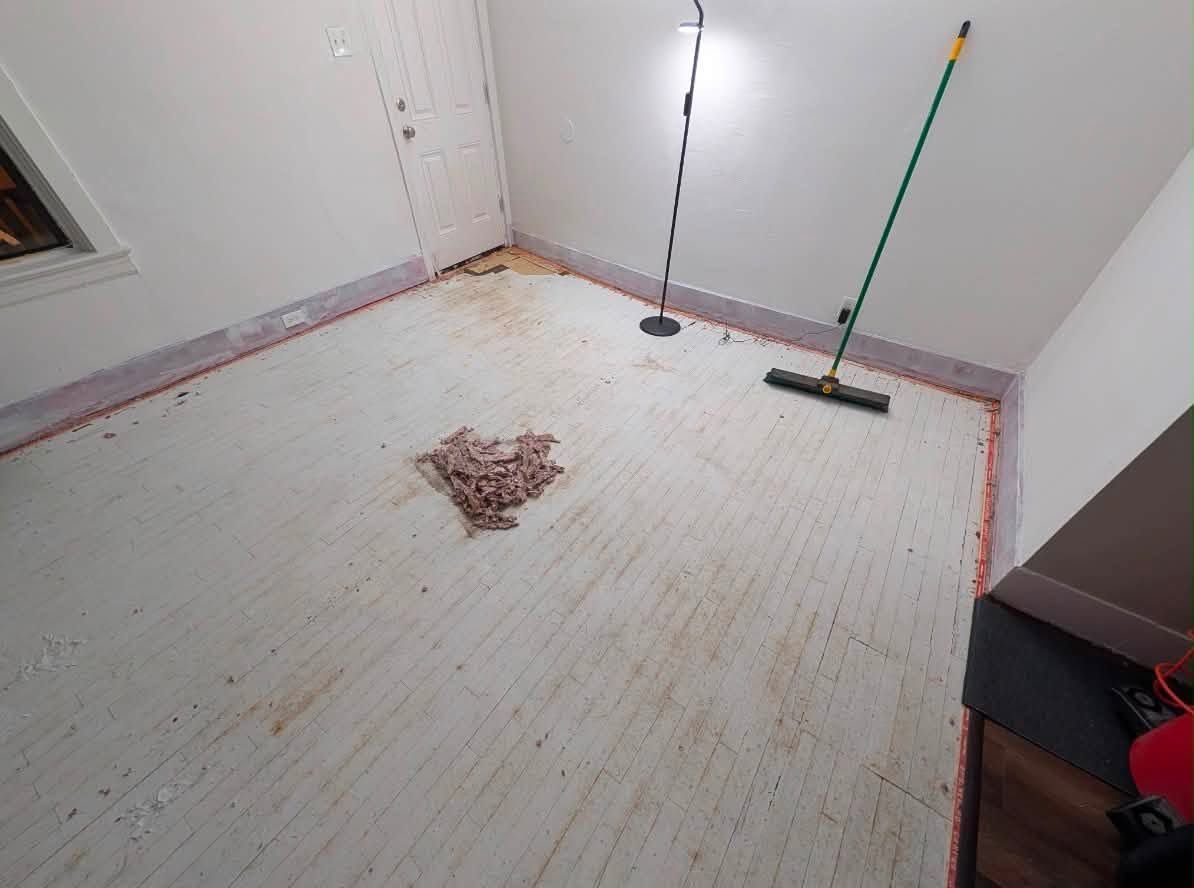 Empty room with white walls, bare floor, and a broom and mop leaning in the corner.