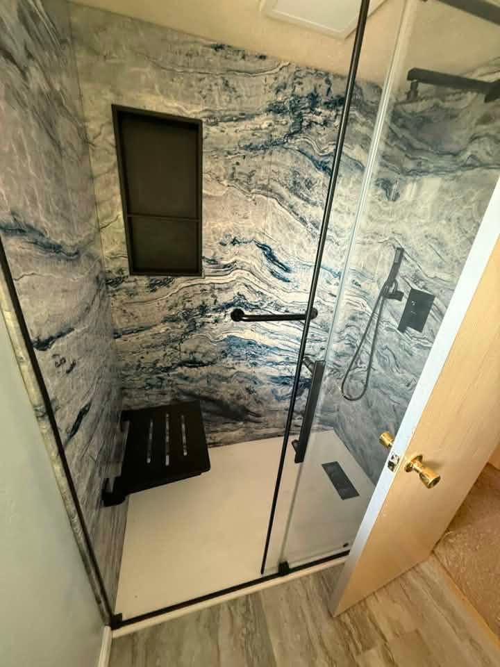 Modern glass shower with marble-pattern tile, black fixtures, and a small window.