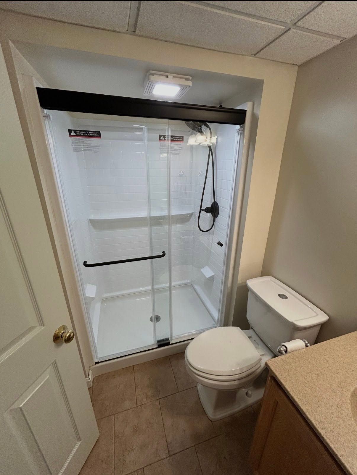 Small bathroom with a glass shower, toilet, sink counter, and beige tile floor.