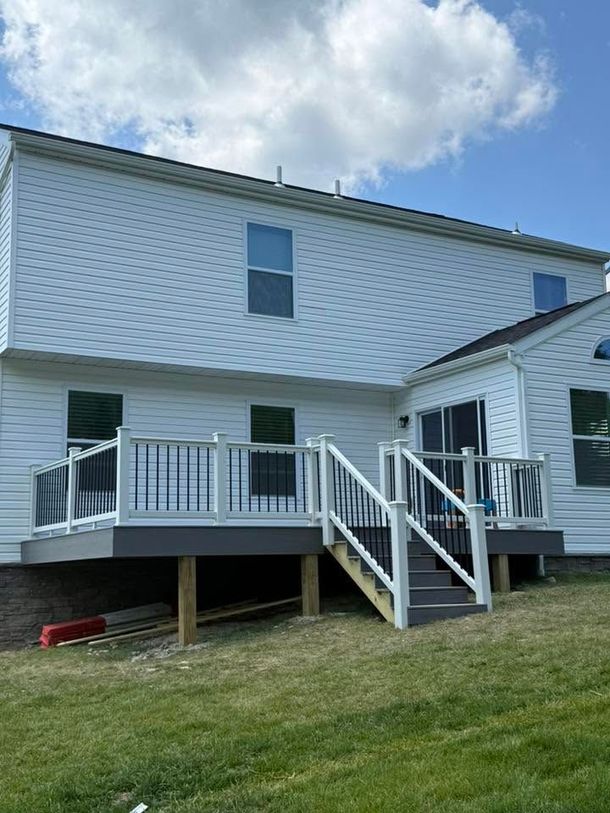 White two-story house with raised backyard deck, stairs, and railing under a blue sky