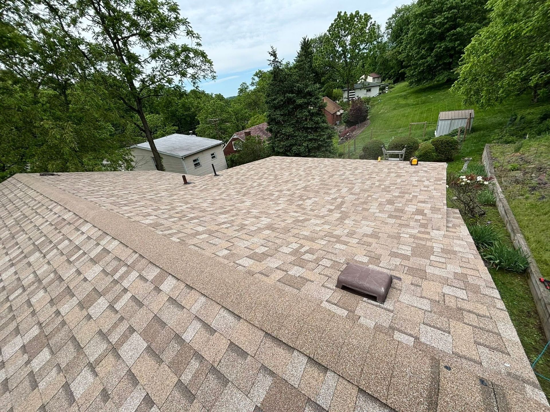 Roof shingles on a house, with a wooded hillside and yard in the background