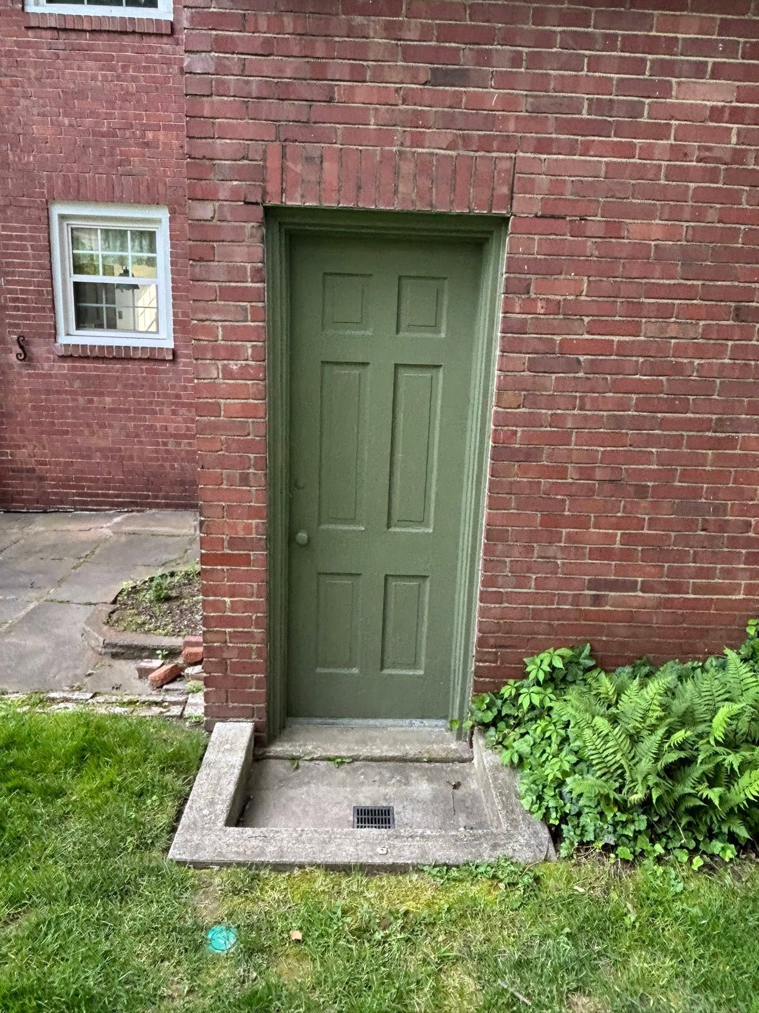 Green door set in a red brick wall with a small window and concrete step in front.