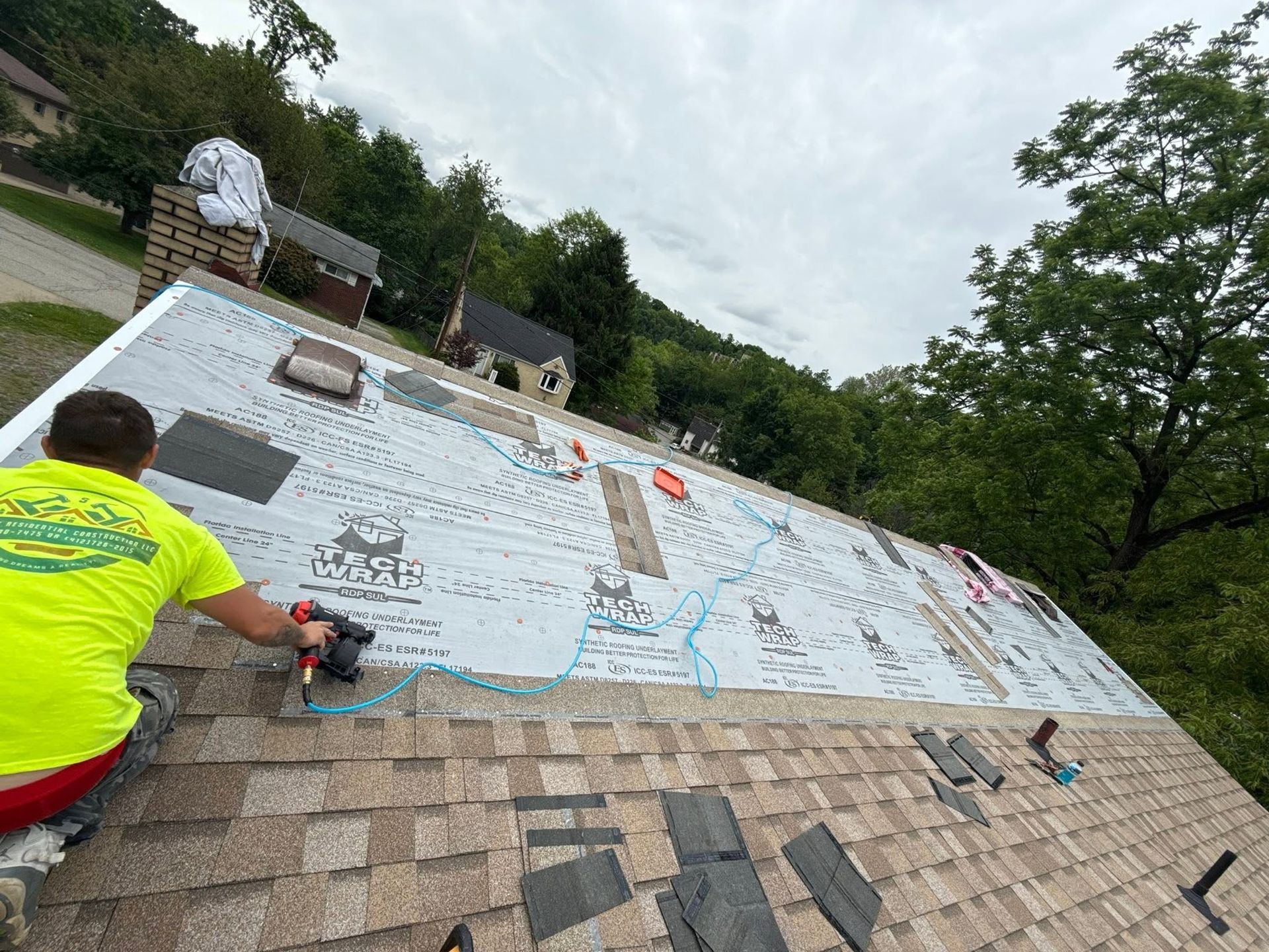Workers installing roofing underlayment on a steep roof, with tools and shingles visible.