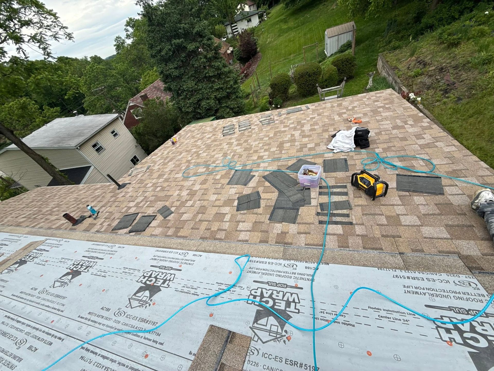 Roofing materials laid on a house roof, with a worker’s tools and tarp in the foreground.