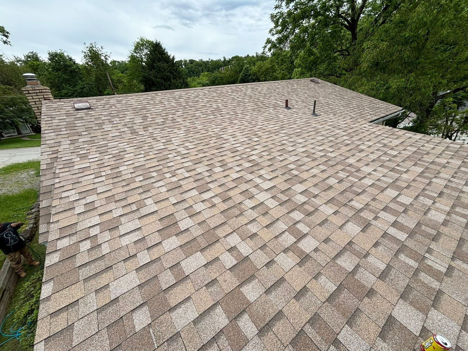Large beige shingled roof with two roof vents, seen from above near trees and grass