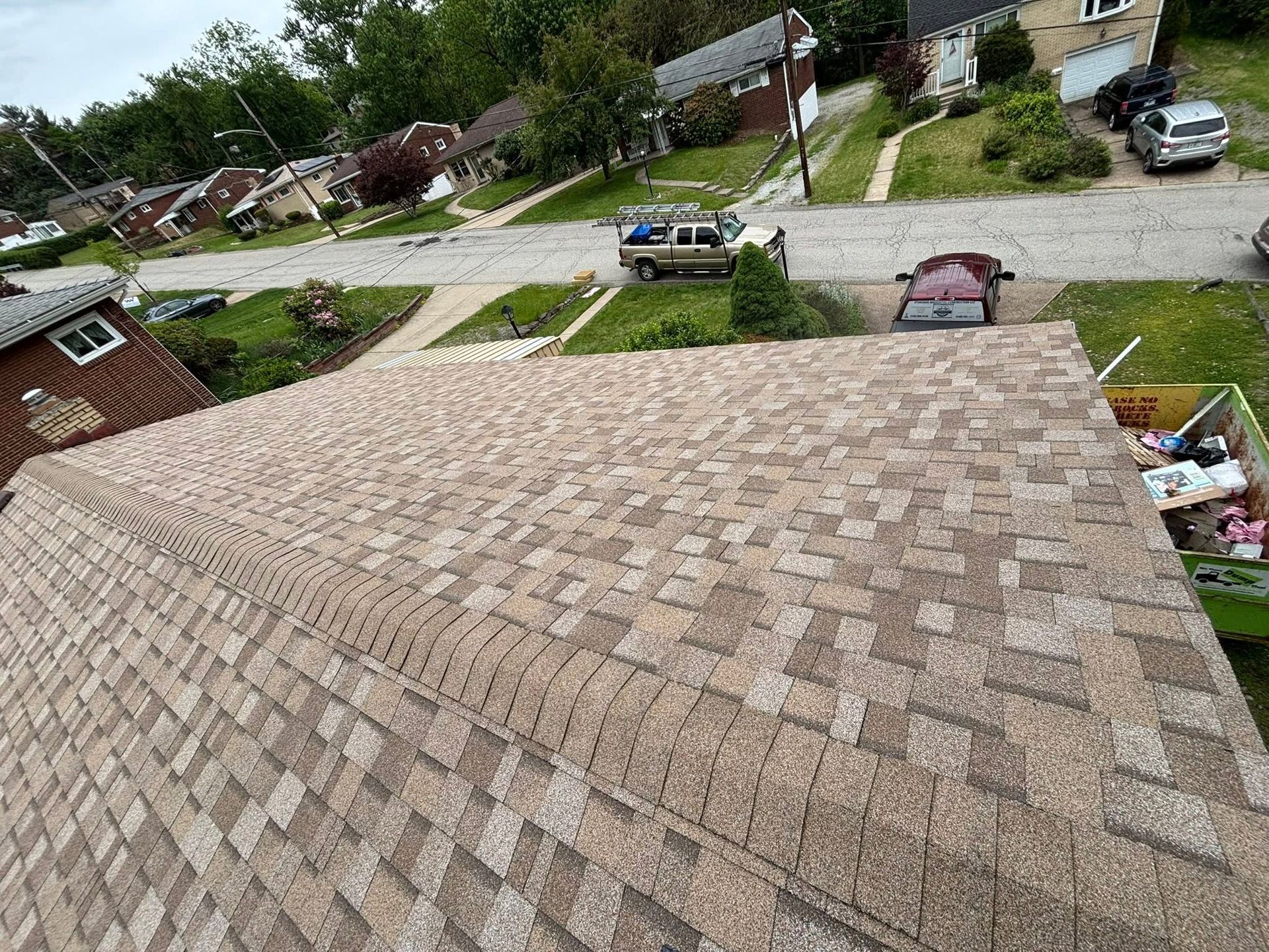 Rooftop shingles viewed from above, with a suburban neighborhood and parked cars in the background