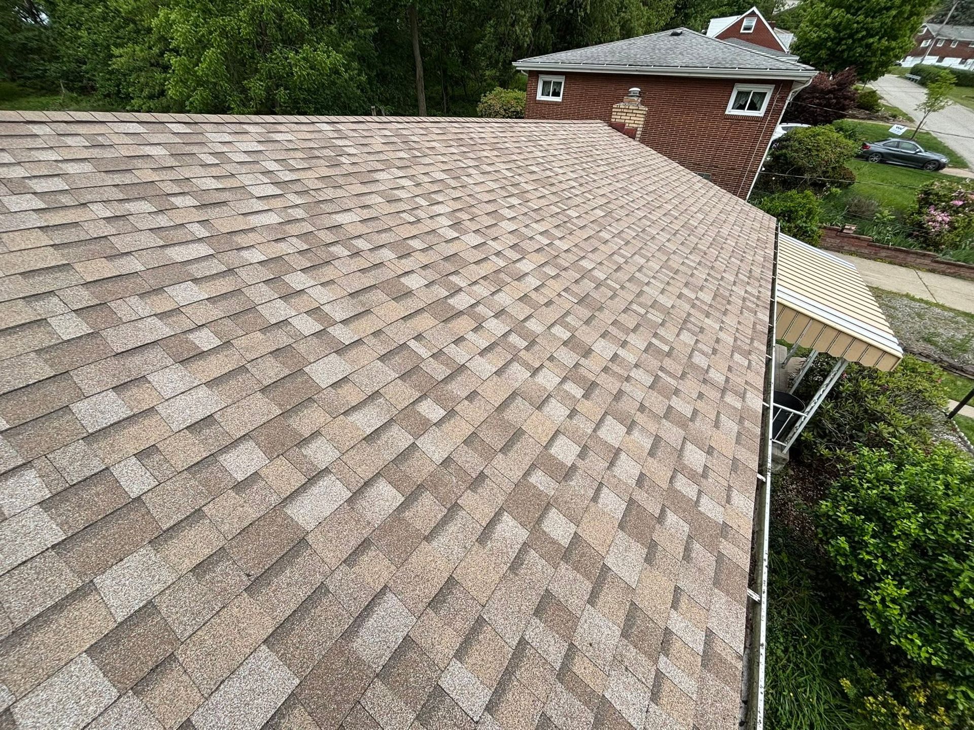 Rooftop covered in weathered shingles beside a brick tower and surrounding trees
