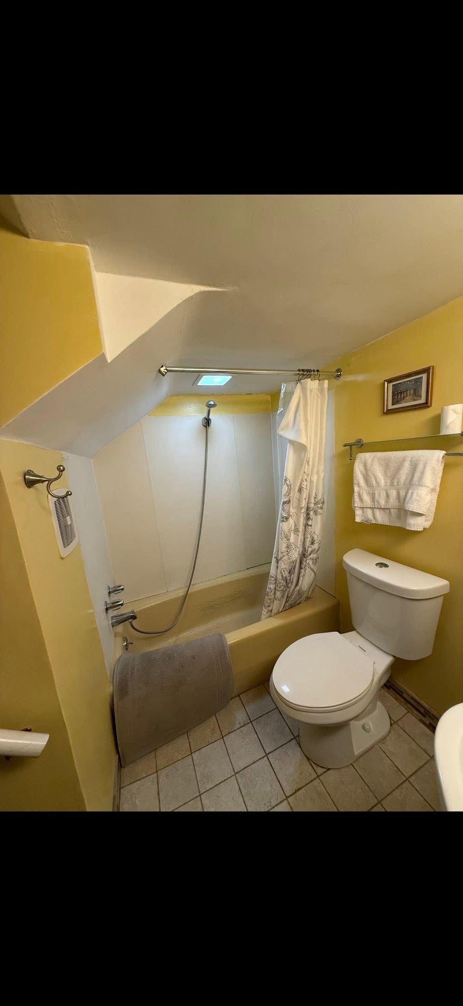Small bathroom with yellow walls, white toilet, sink, towel, and a shower stall with tiled floor.
