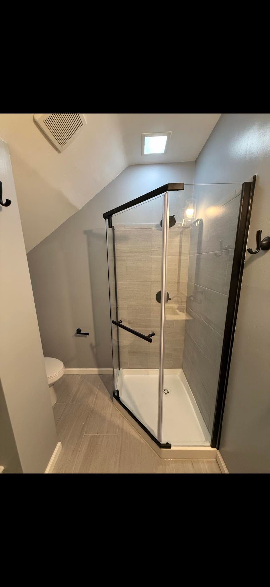 Small bathroom with glass shower enclosure, white walls, and tiled floor under a skylight.