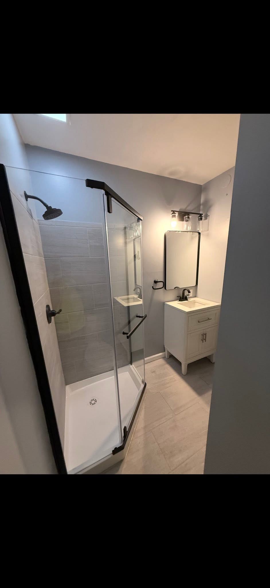 Modern shower room with white tile, black shower fixtures, and a wall-mounted sink.