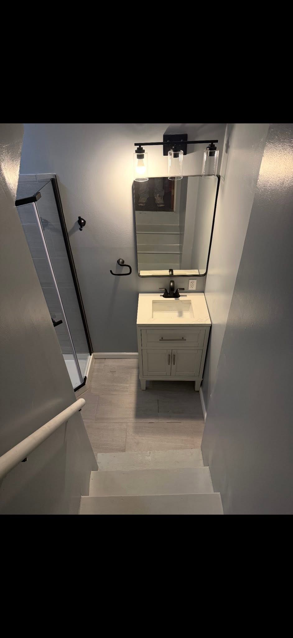 Narrow bathroom with a white vanity, mirror, wall light, and gray tile floor under a sloped ceiling