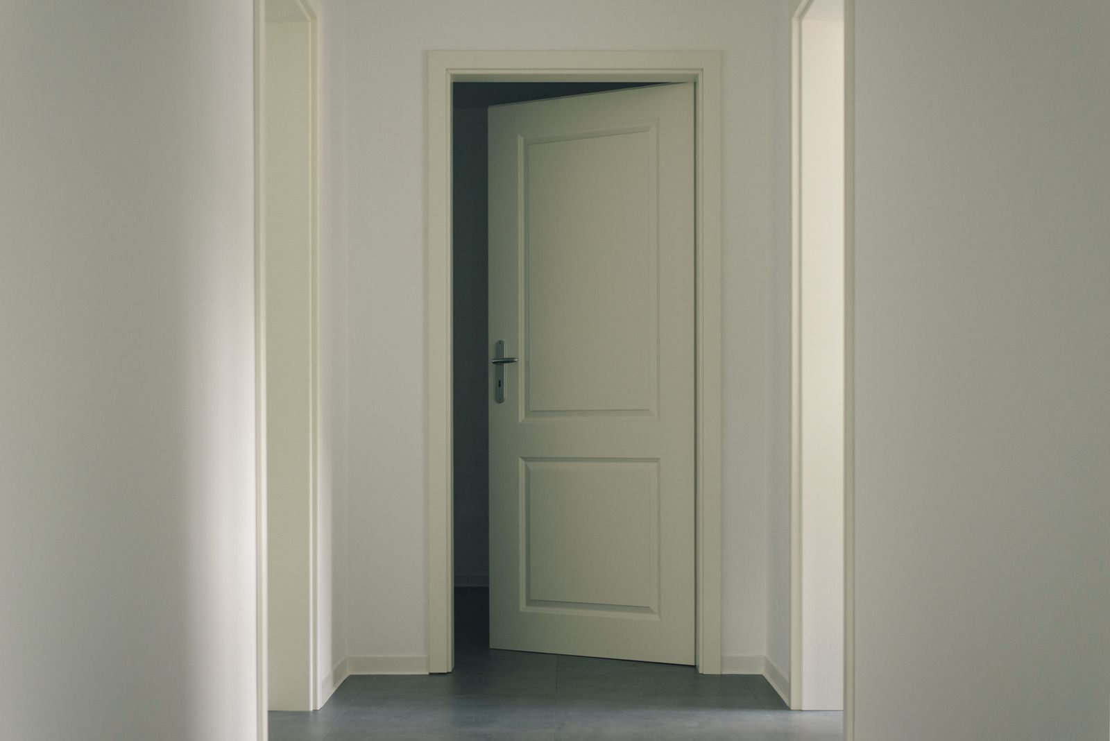 Open white door in a pale hallway with gray floor tiles