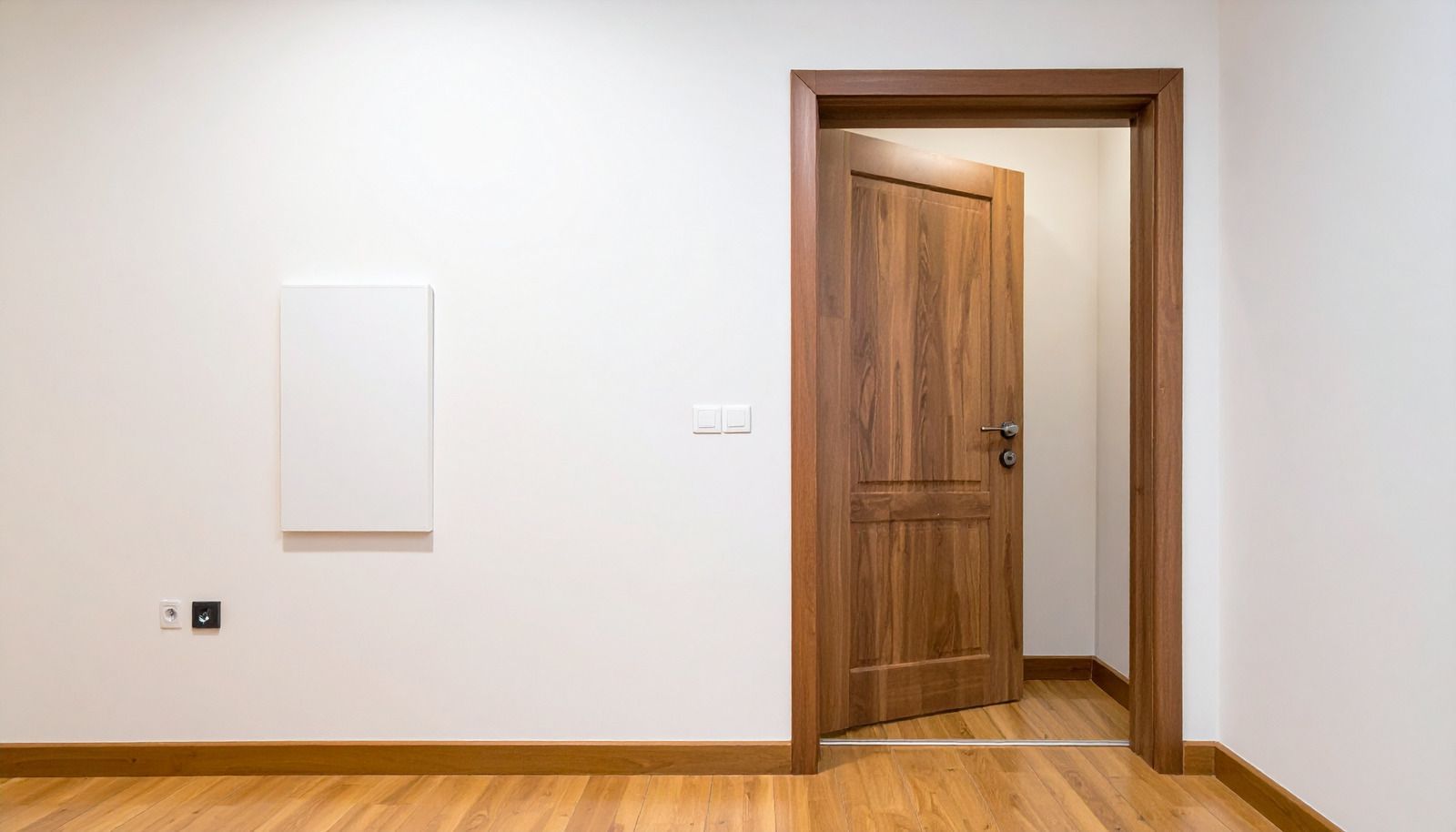 Minimal white room with wooden floor and open wooden door to a hallway