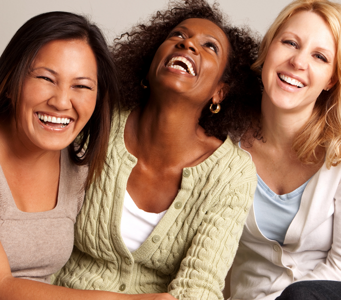 Three women are laughing together and one is wearing a green sweater