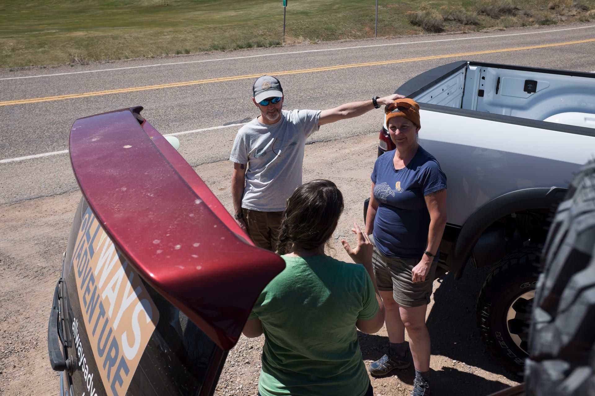 Three people beside a pickup truck. One points at the truck’s red spoiler. The other two look on.