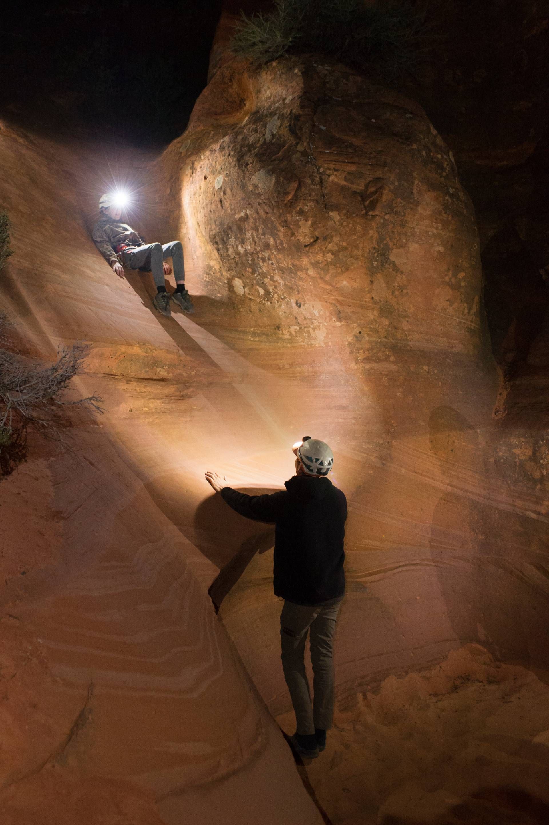 Two people wearing helmets and harnesses stand in a narrow slot canyon.