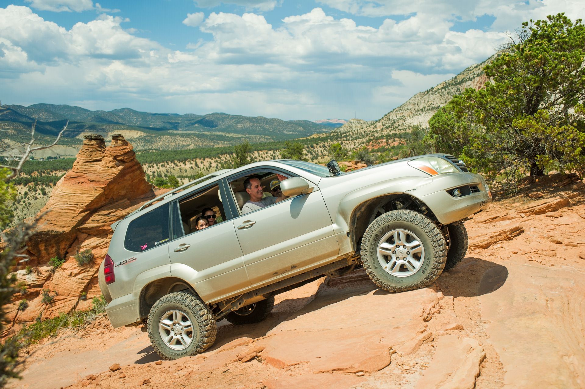 SUV driving up a rocky, off-road path in a desert landscape. A man and children are in the vehicle.
