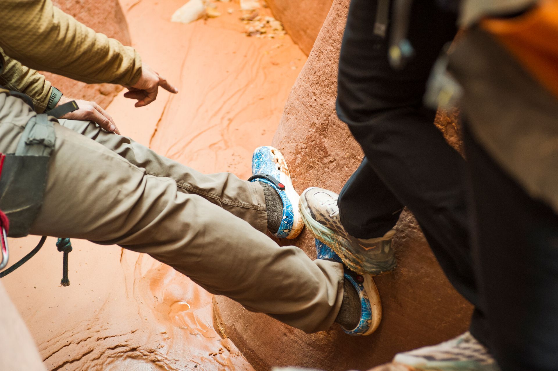 Two climbers’ legs and blue shoes bracing on a narrow, orange canyon wall