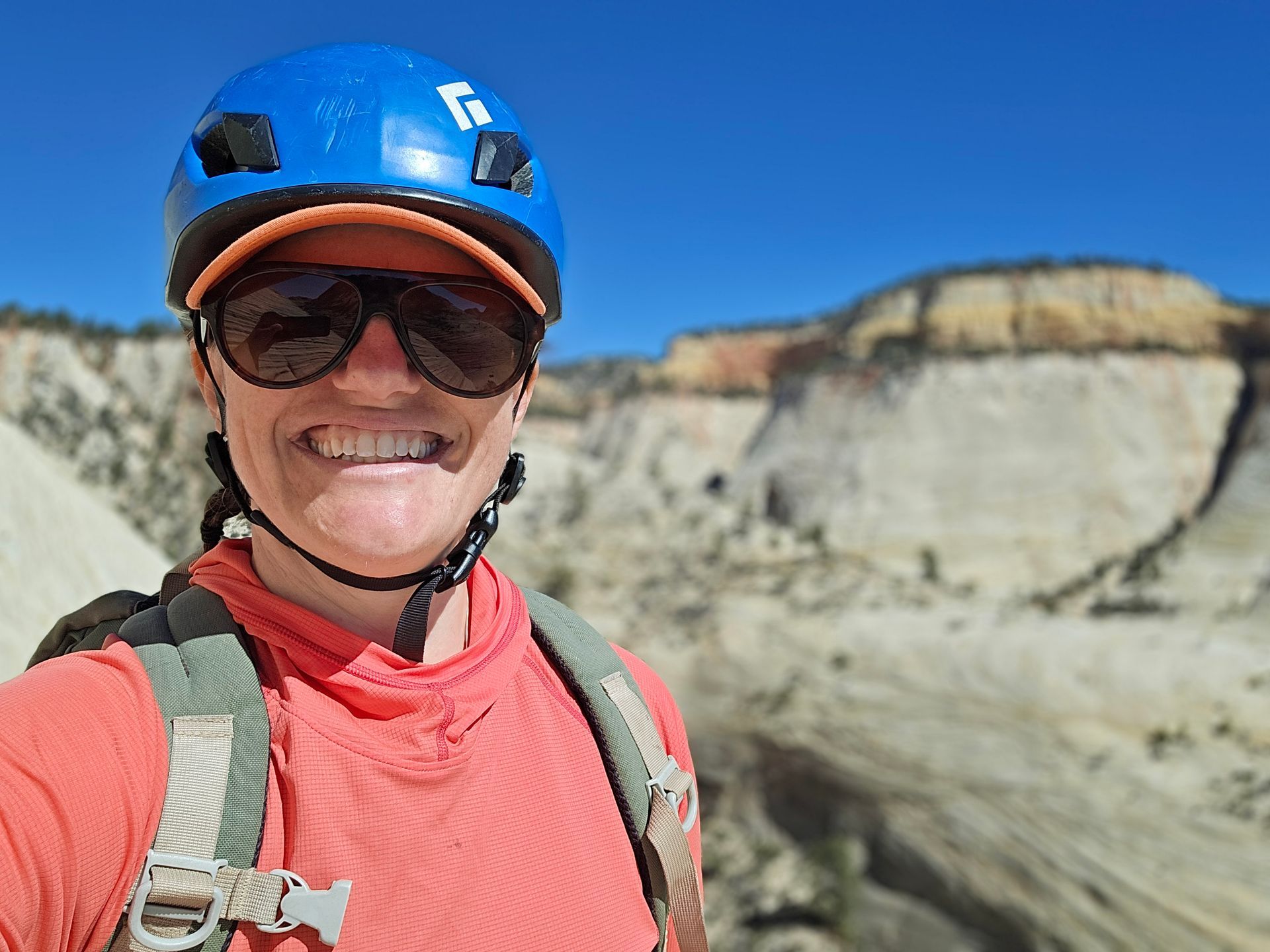 Smiling person wearing sunglasses and a helmet in a canyon setting.