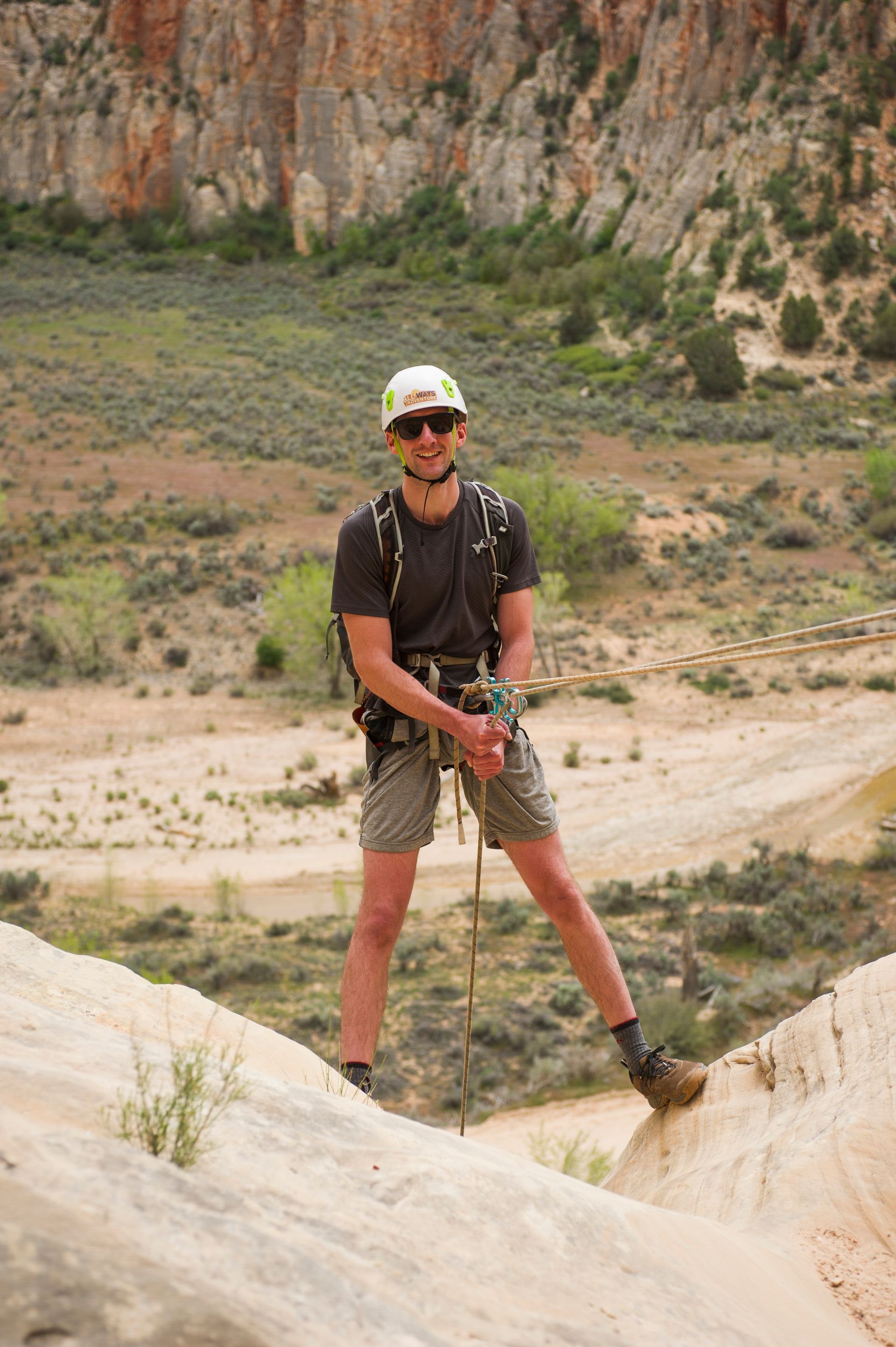 Person standing on a rocky trail in a desert canyon, holding a camera with a strap.