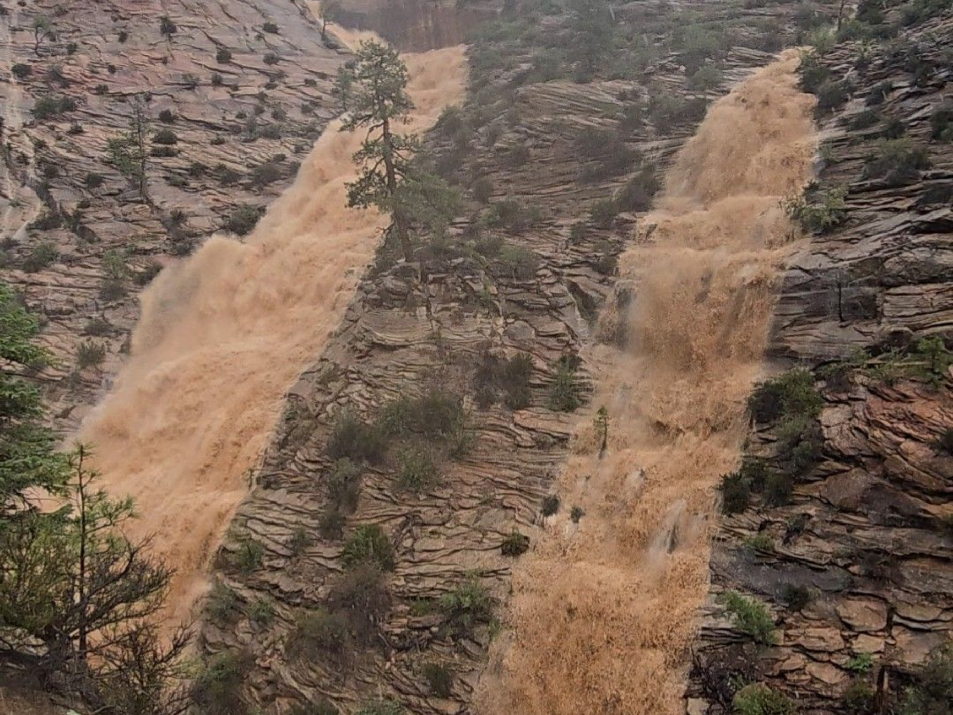 Two muddy waterfalls rushing down a rocky hillside in a barren landscape