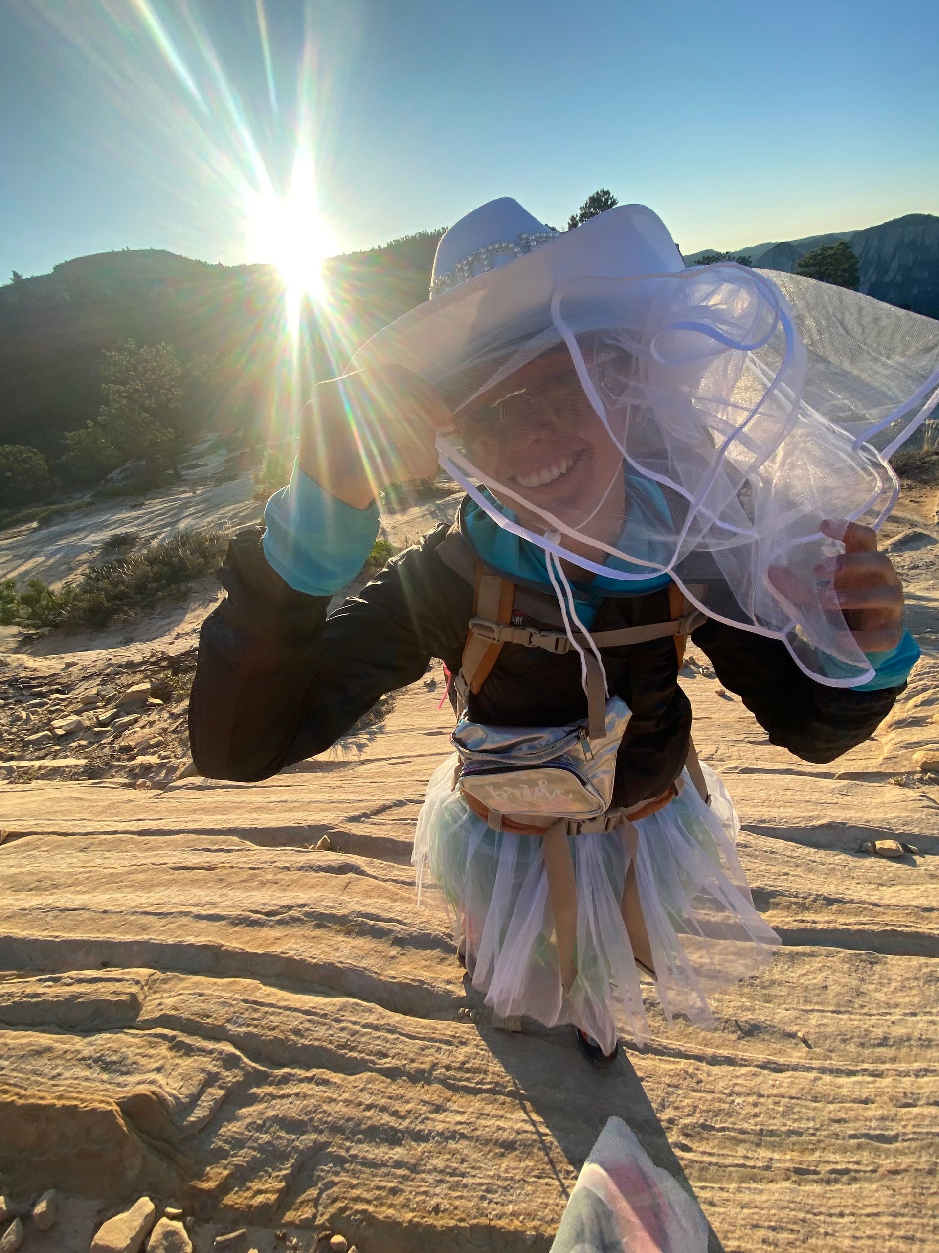 Person hiking on a sunlit mountain trail, carrying a large white bundle on their back