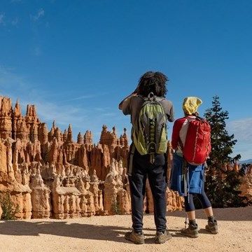 Two hikers with backpacks overlooking orange rock formations under a blue sky.