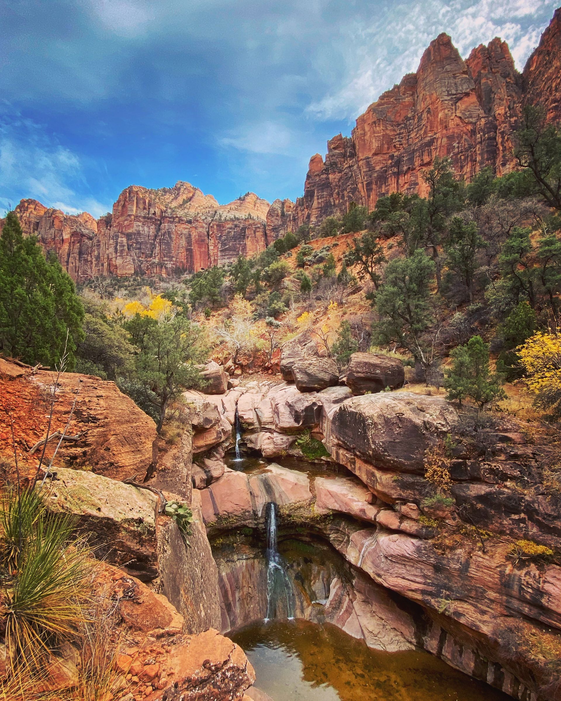 Waterfall cascading into a pool amidst red rock canyon with blue sky backdrop.