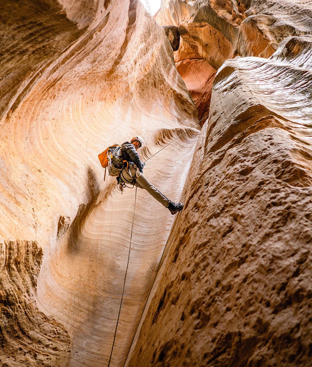 Person rappelling down a narrow sandstone canyon.