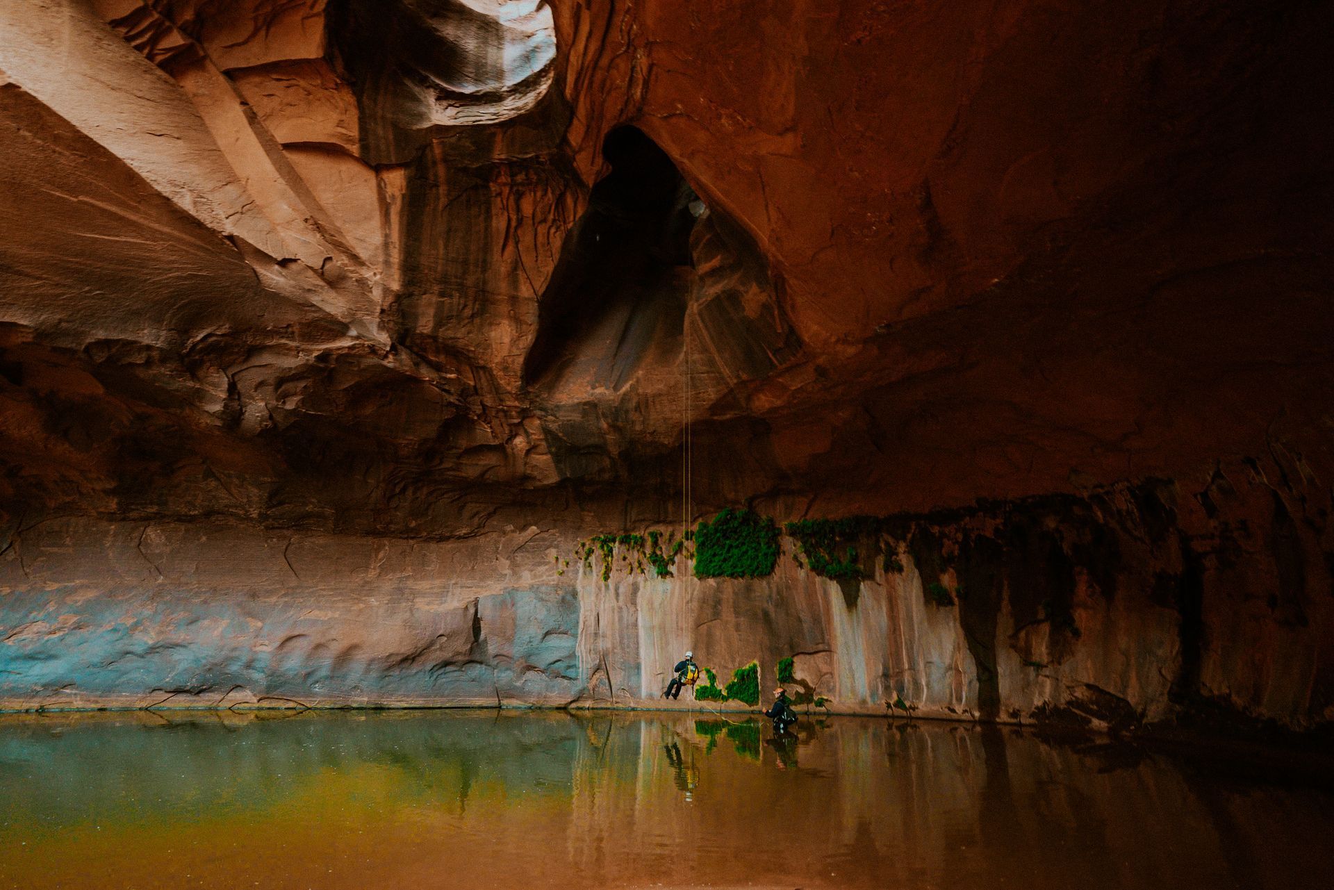 A person is standing in a cave next to a body of water.