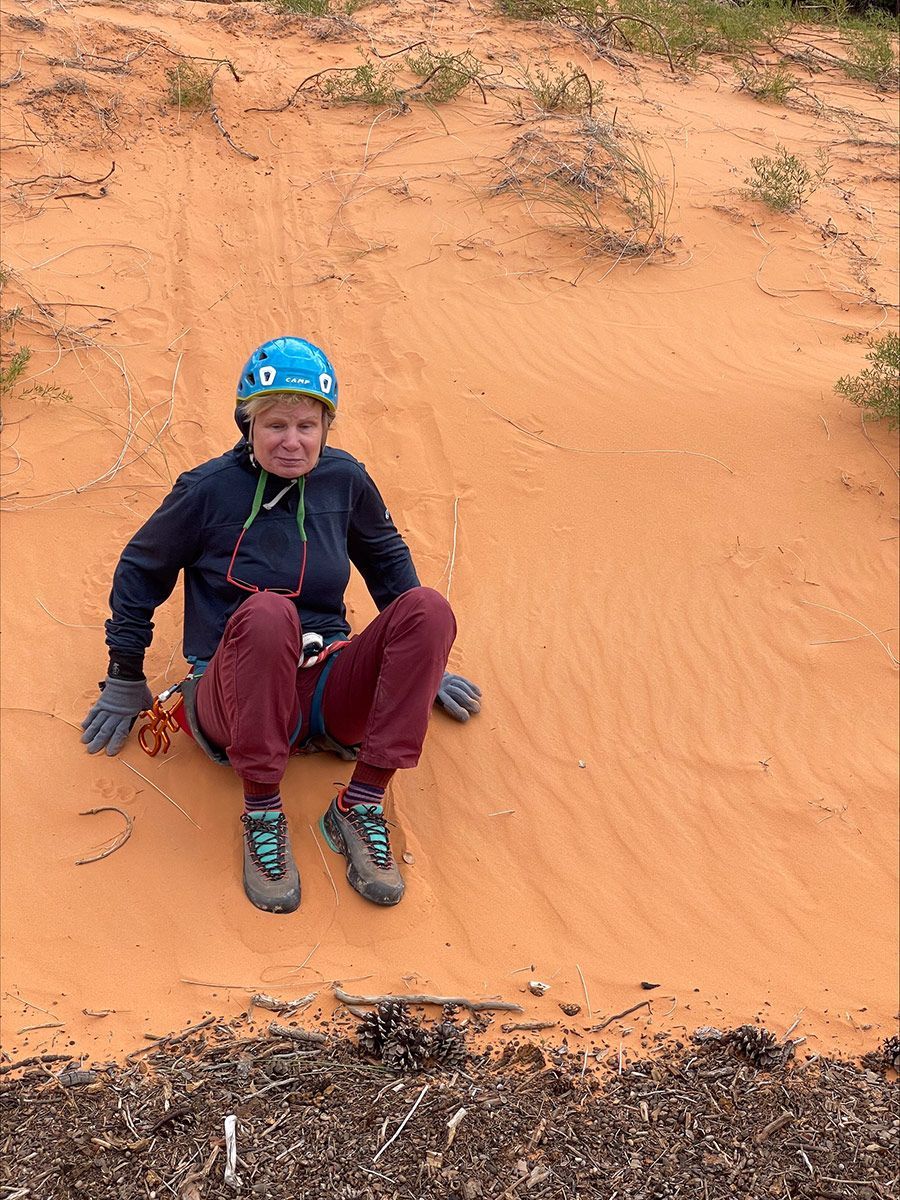 Person in blue helmet and dark clothes sits on a red sand dune.