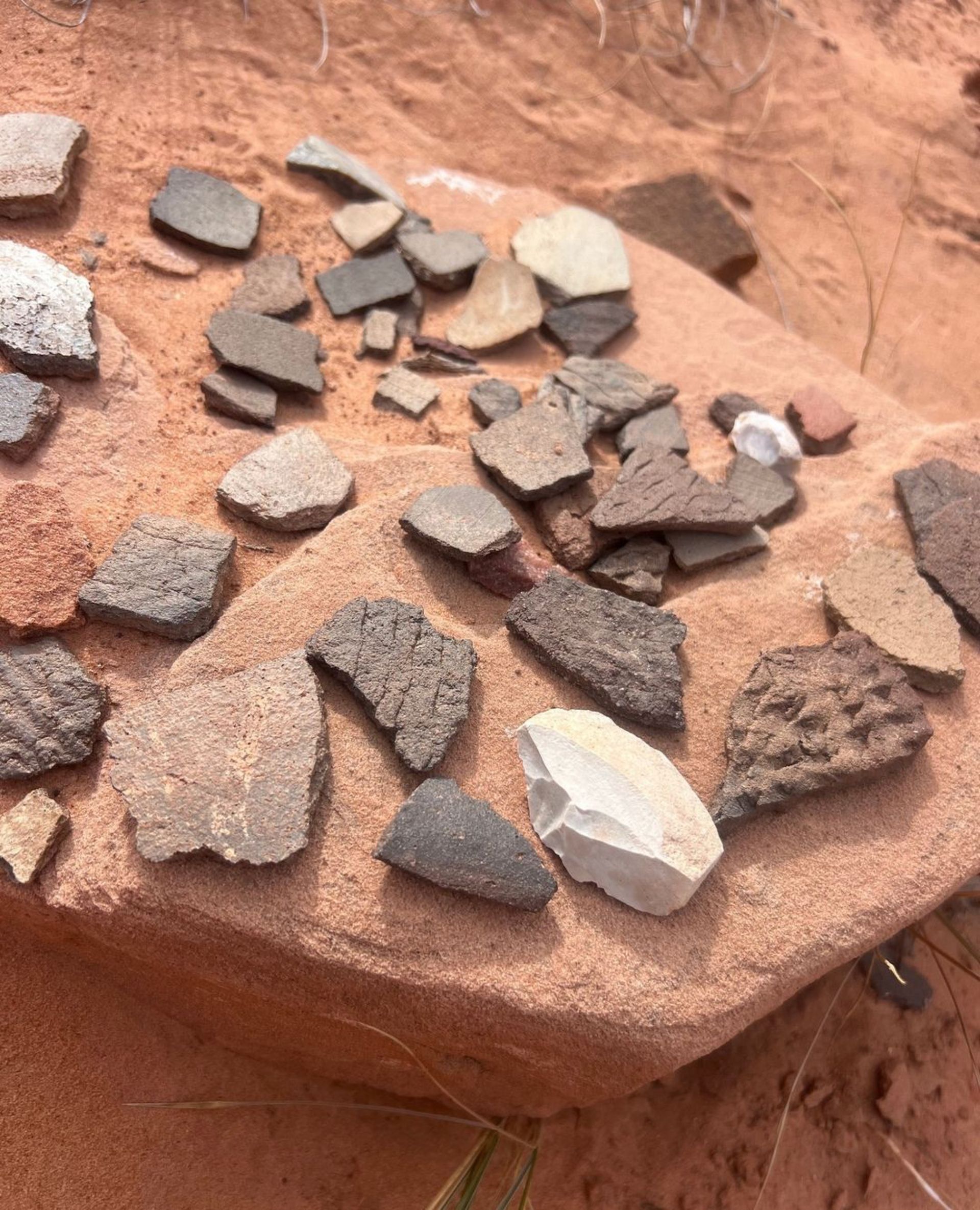 Scattered pottery shards on a red rock in a desert landscape.