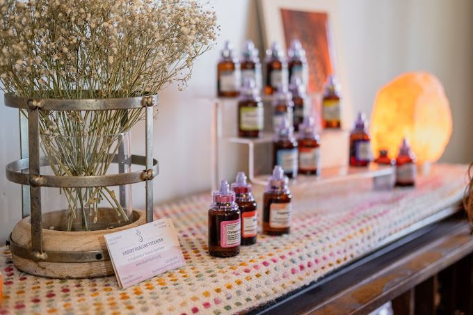Display of aromatherapy bottles on a table, with dried flowers, a glowing salt lamp, and a colorful tablecloth.
