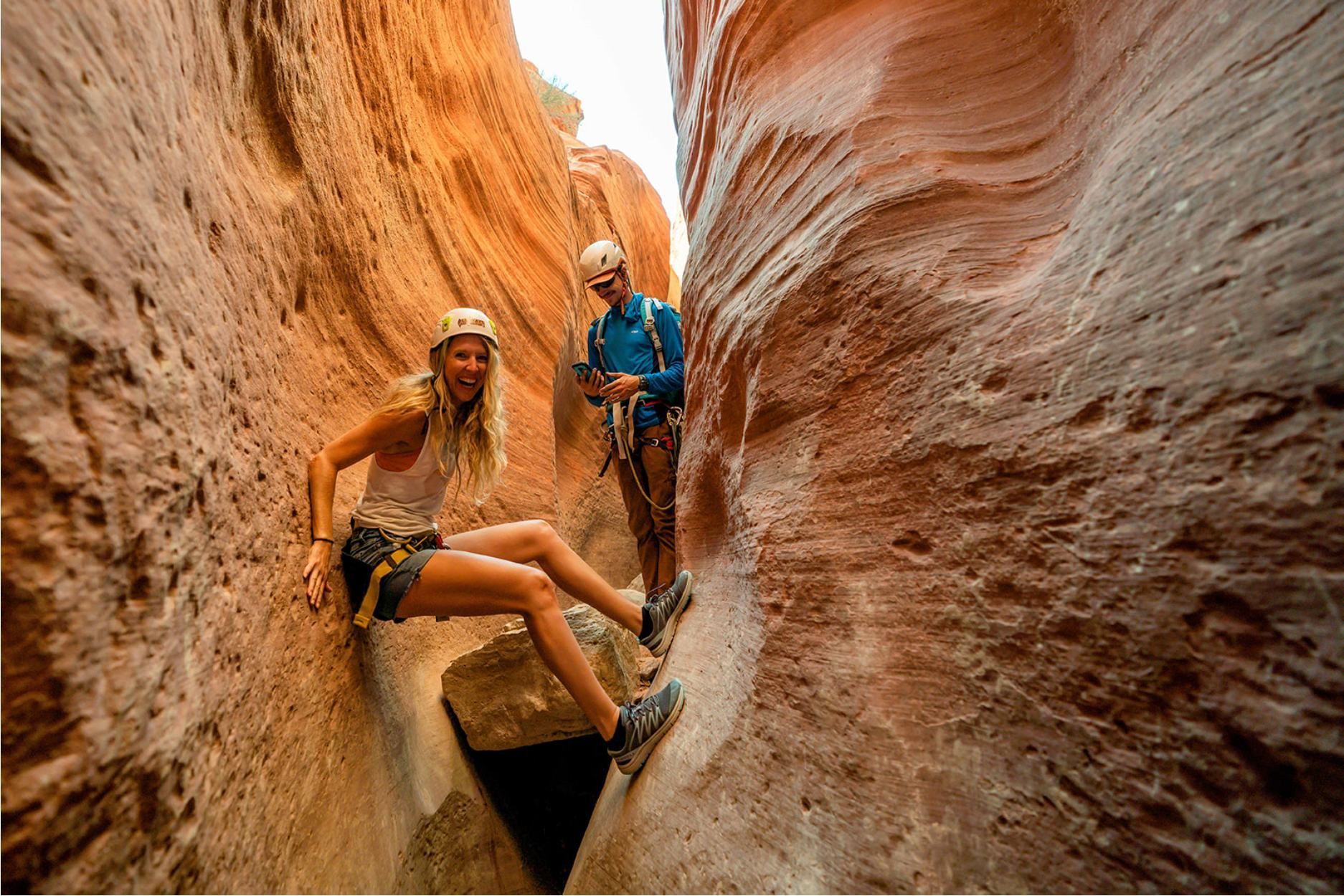 Woman descending a narrow sandstone canyon on a rope; another person looks on.