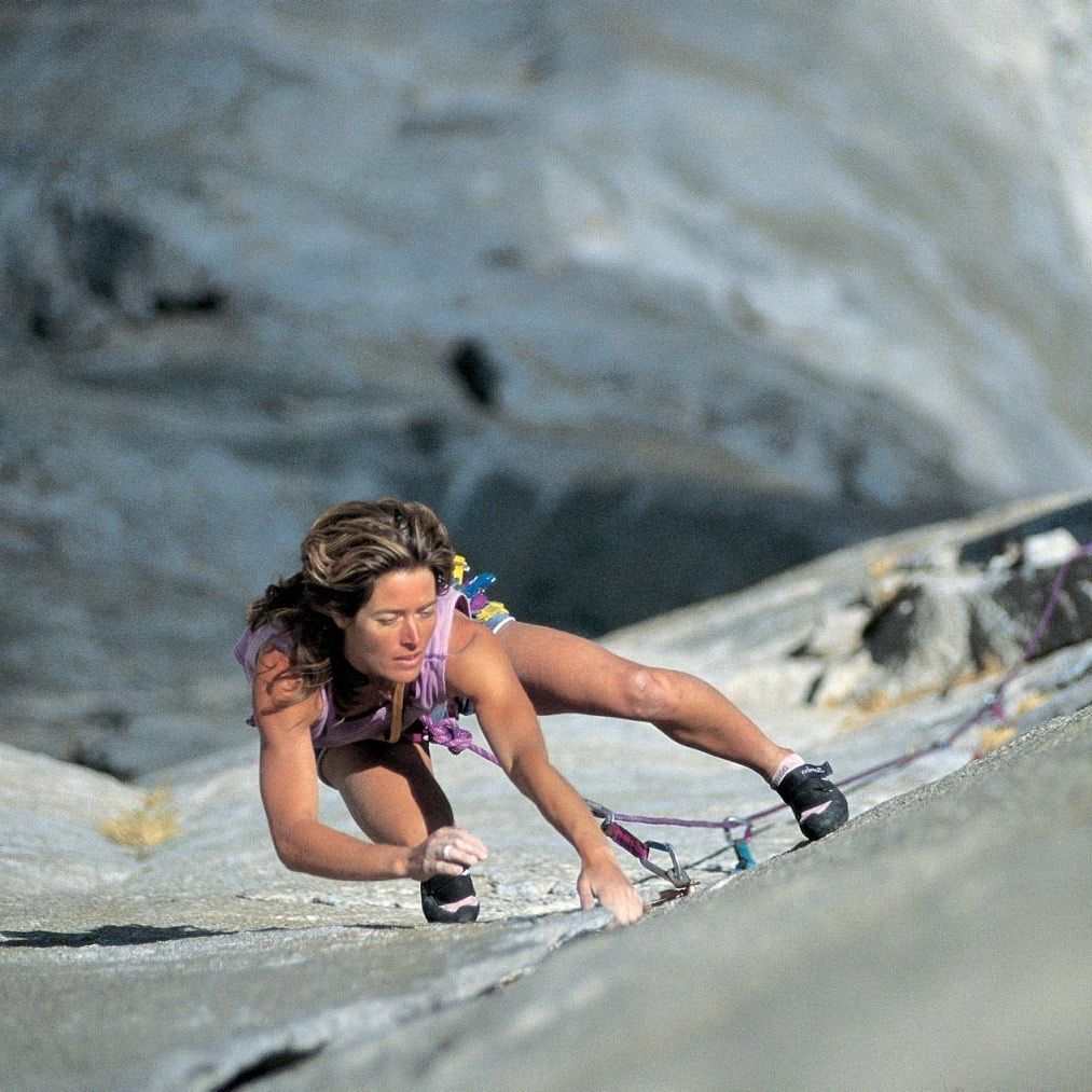 Woman rock climbing on a steep, light-colored rock face, using ropes for safety. She is focused.